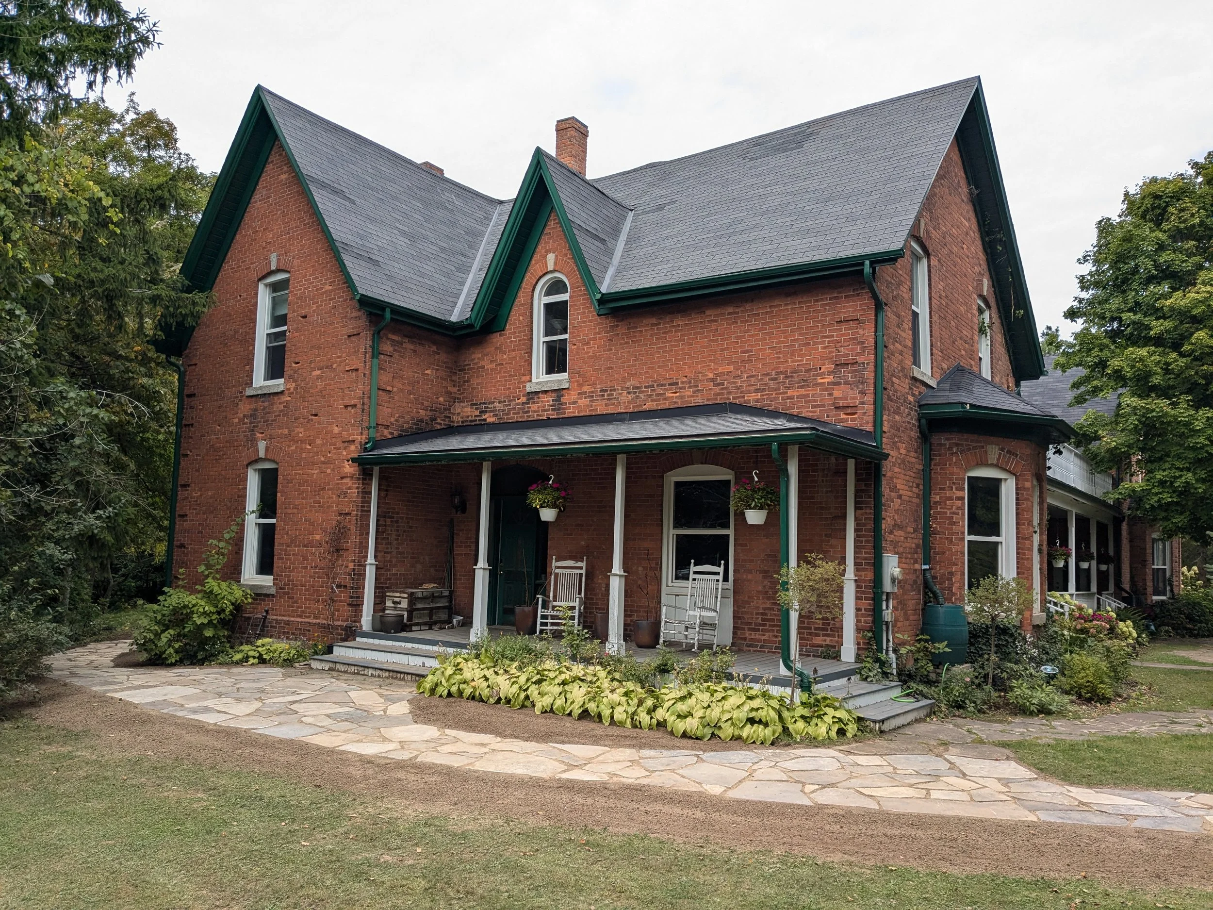 Professional landscaping featuring a custom flagstone path, and perennial garden borders surrounding a two-story brick farmhouse in Grimsby