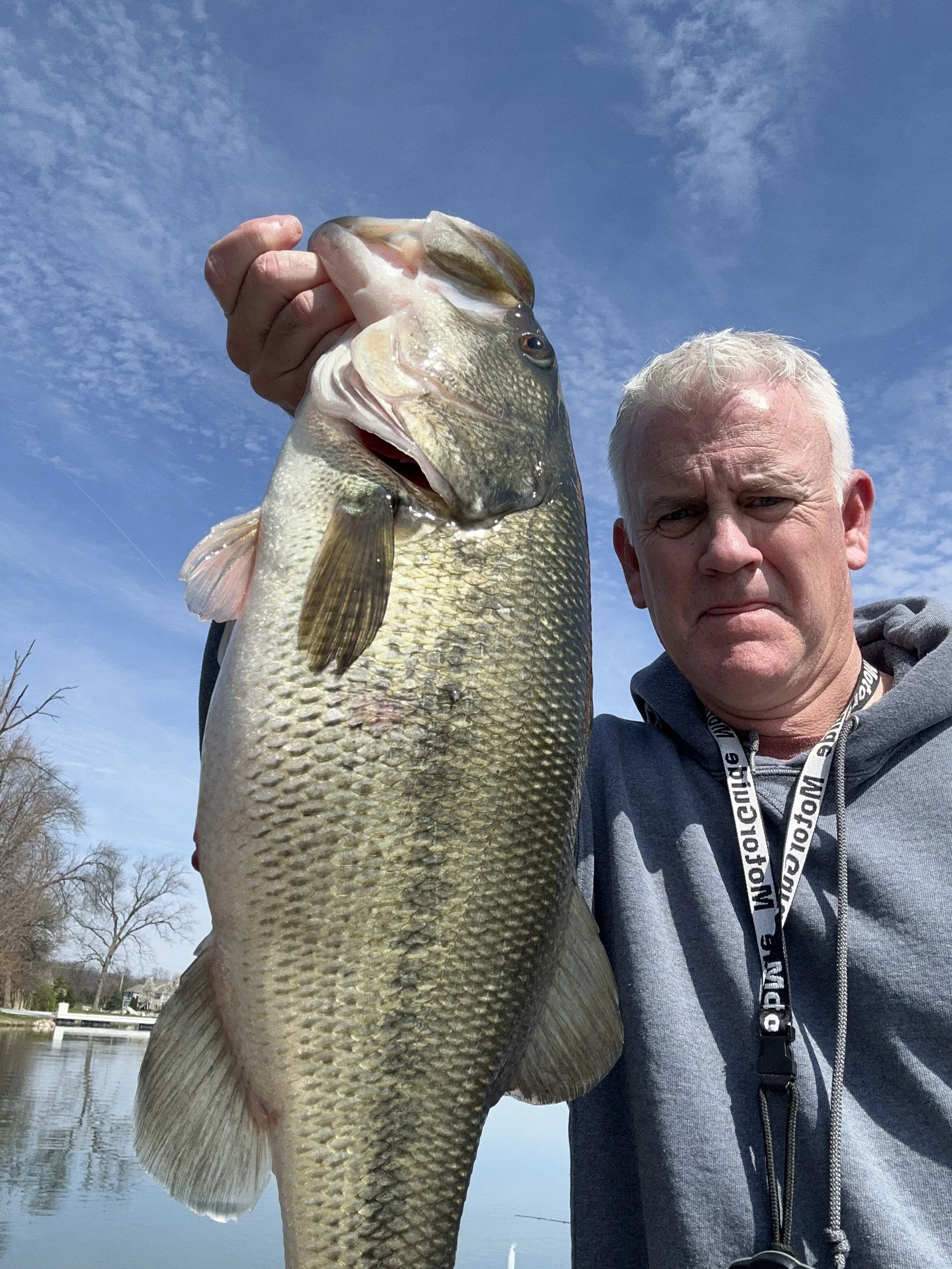 Fisherman with a 6-pound largemouth bass caught in March 2024 on an Indianapolis lake, displayed against a clear sky.