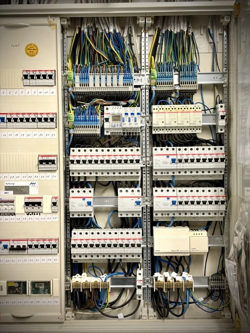 Schaltschrank mit mehreren Sicherungsautomaten, Leitungskabeln und Schaltkomponenten.
