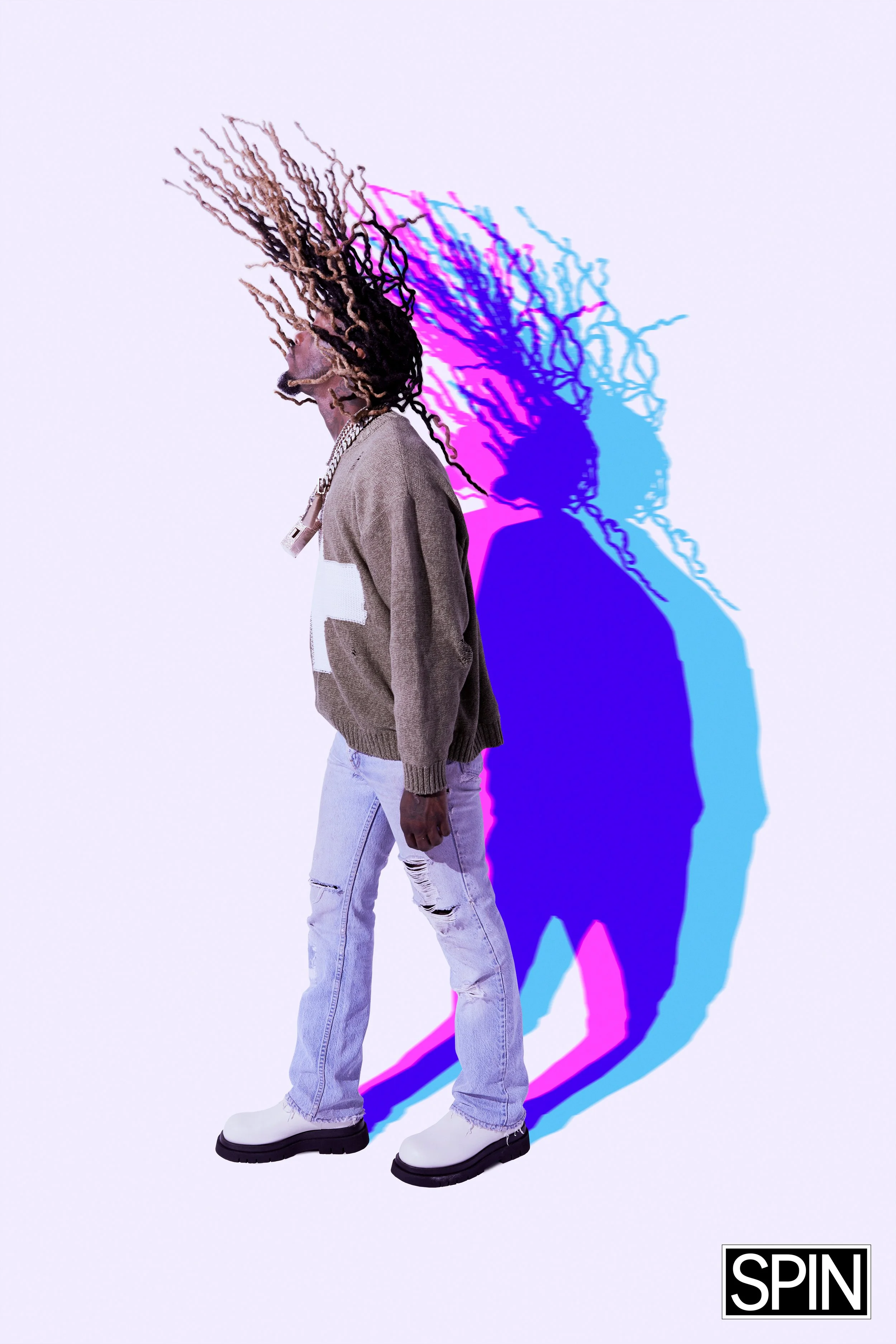 A person with long dreadlocks standing sideways, wearing a beige jacket, ripped jeans, and white boots, casting a colorful shadow against a white background with the SPIN logo in the bottom right corner.