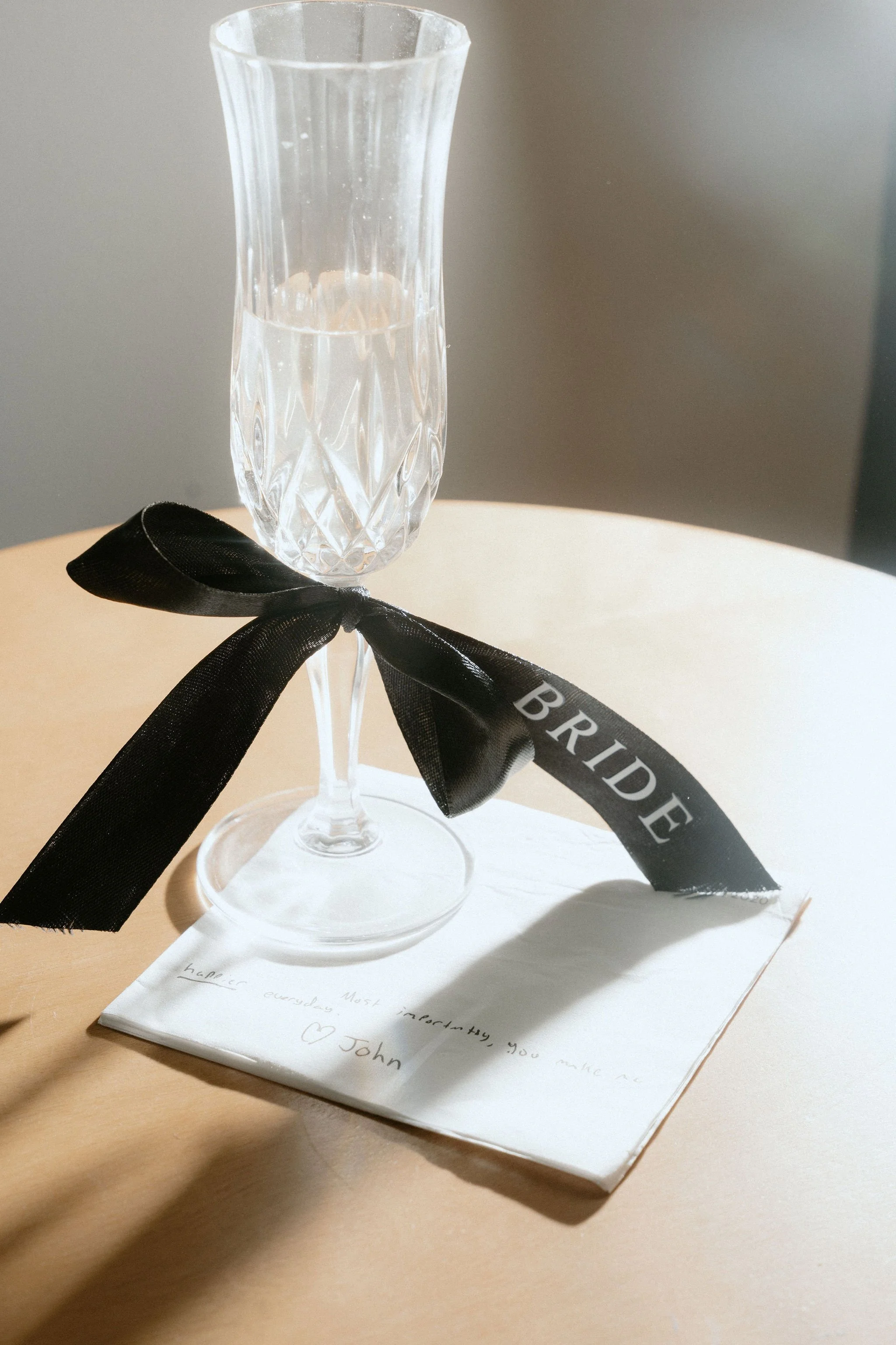 Champagne glass with black ribbon that says bride