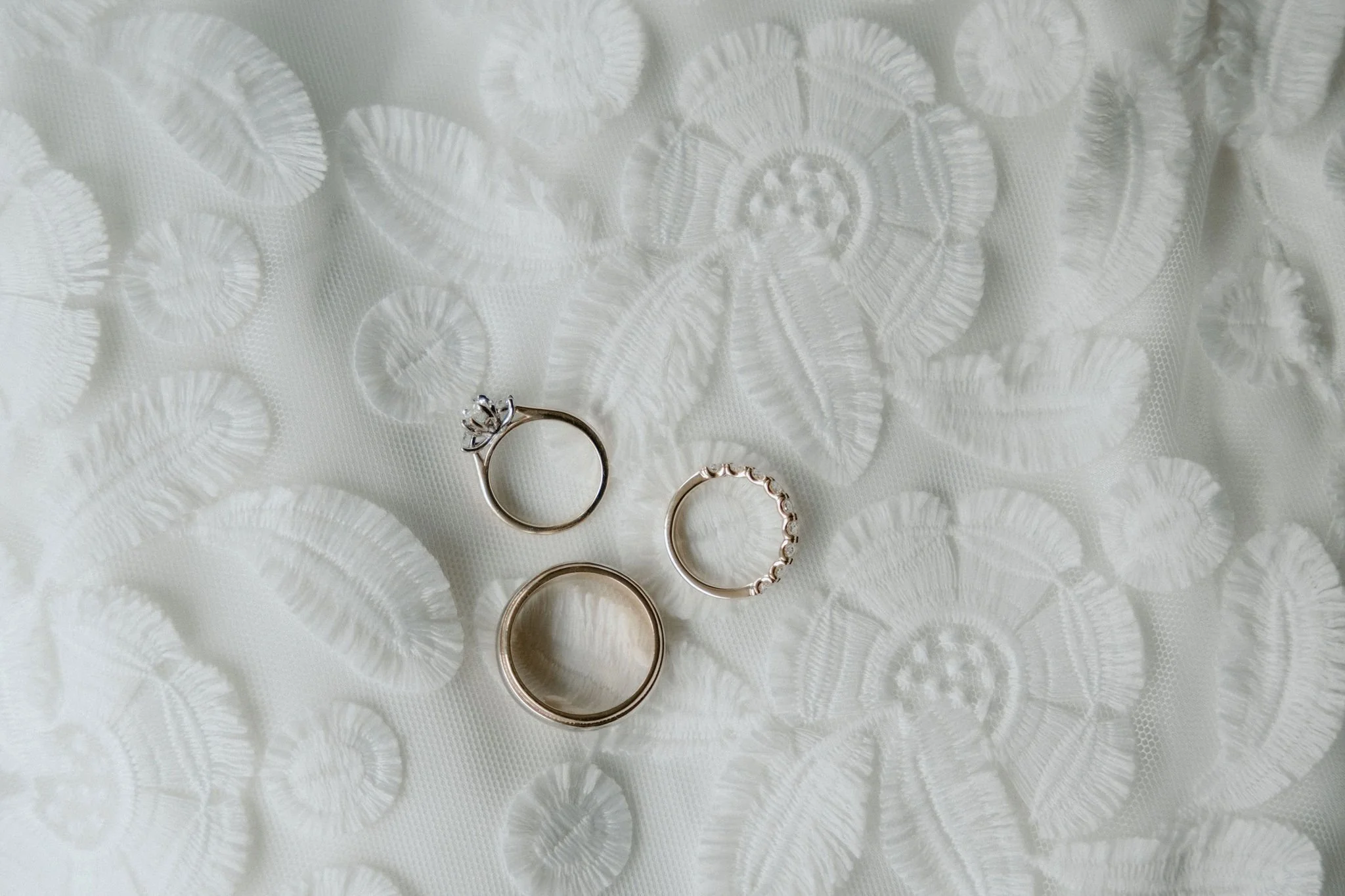 Three rings on a white embroidered fabric with floral and leaf patterns.