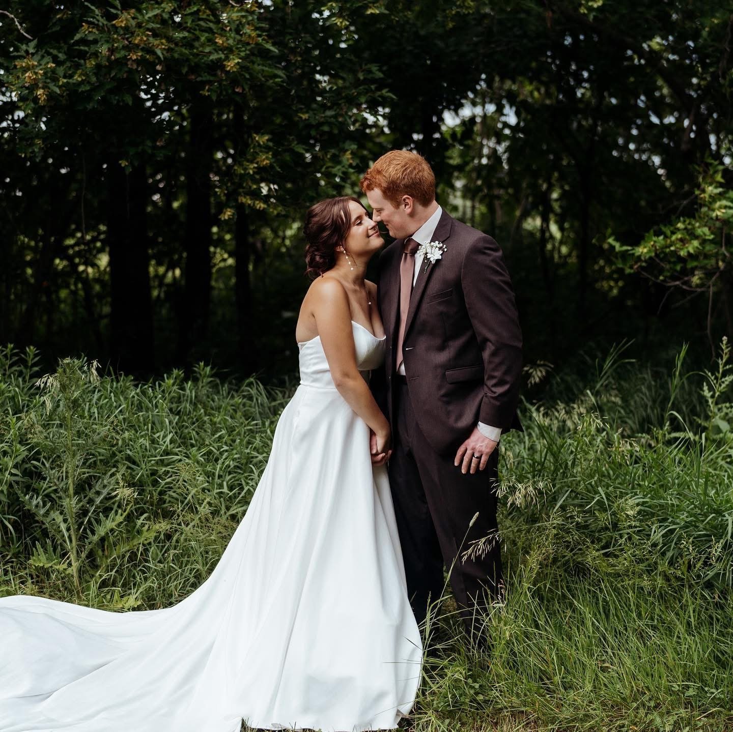 Bride and groom stand in tall green grass smiling at one another on their wedding day photographed by Tonya Hjort