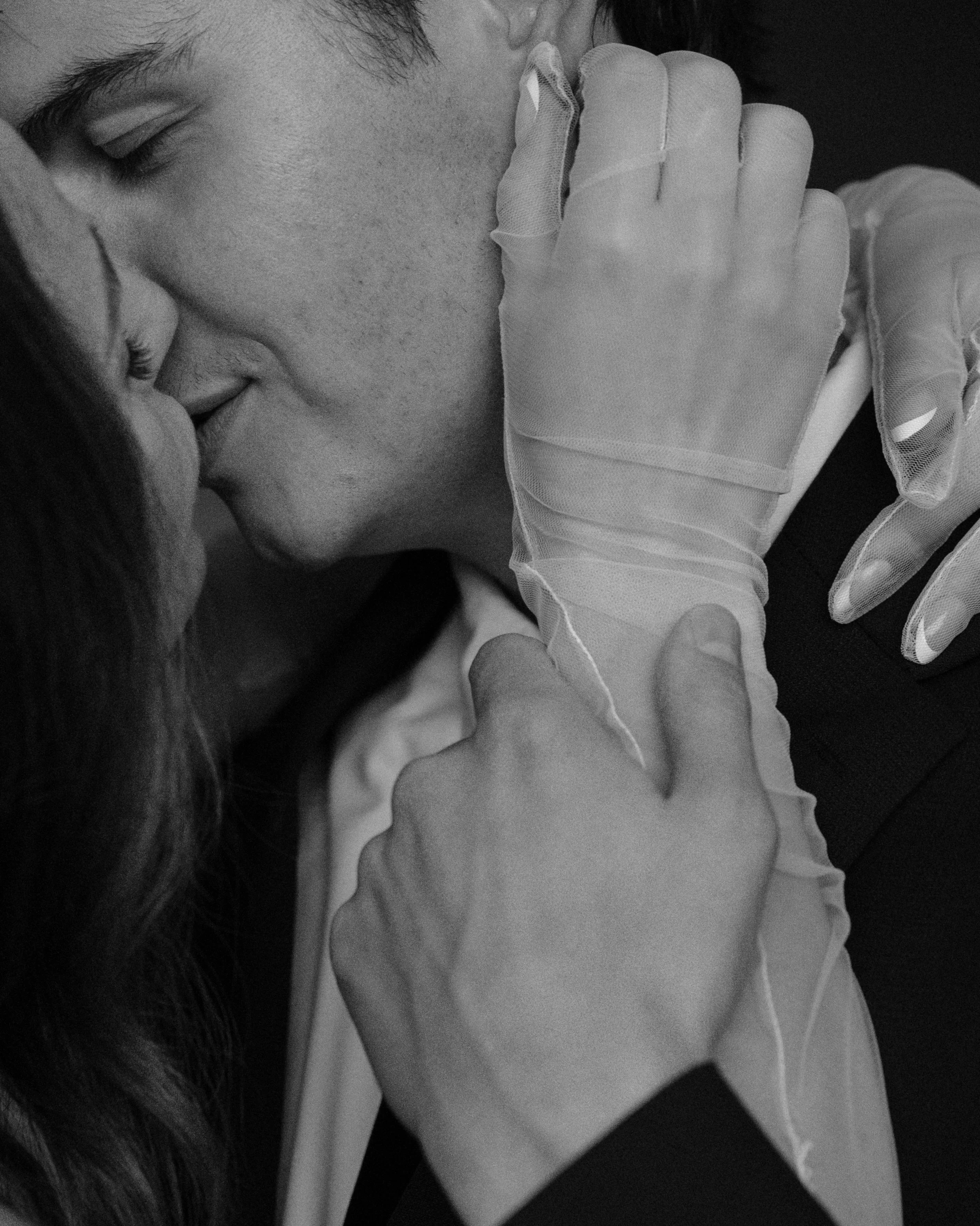 A black and white close-up of a couple kissing, with one person wearing gloves.