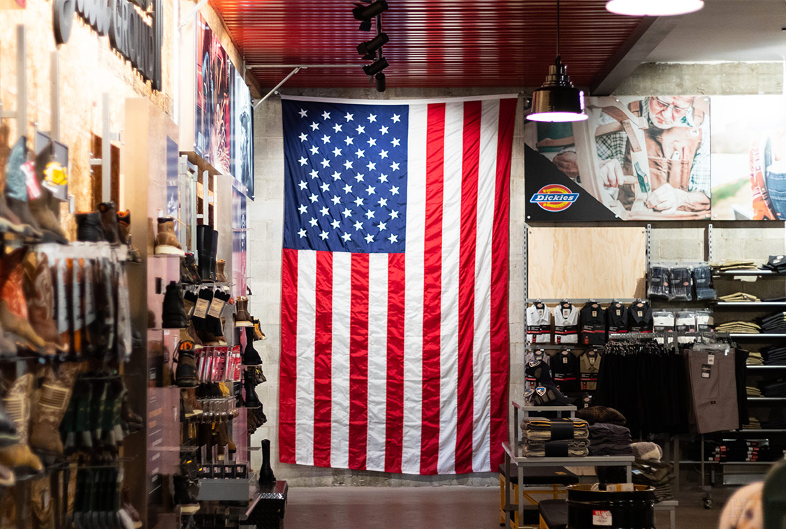 American flag hanging inside a store, with shelves of boots and clothing on both sides.
