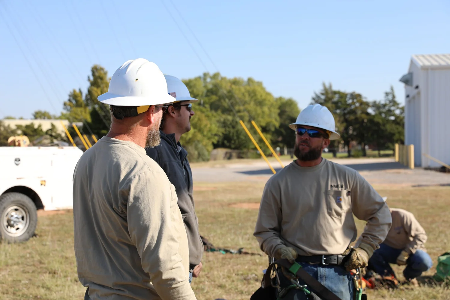 Three NWEC crew members in white hard hats talking outdoors