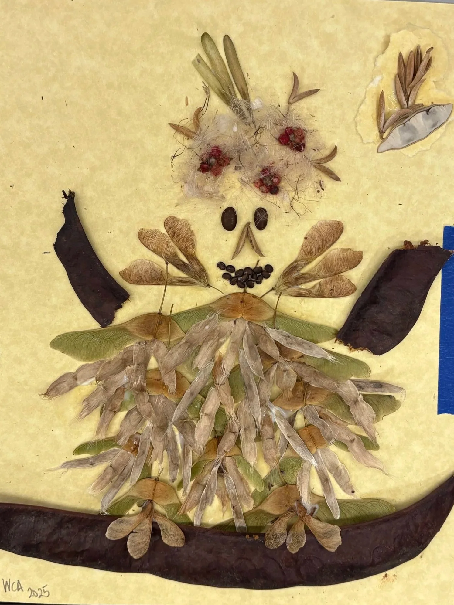 Artistic lion face created with various natural materials like leaves, seeds, and flower petals on yellow background.