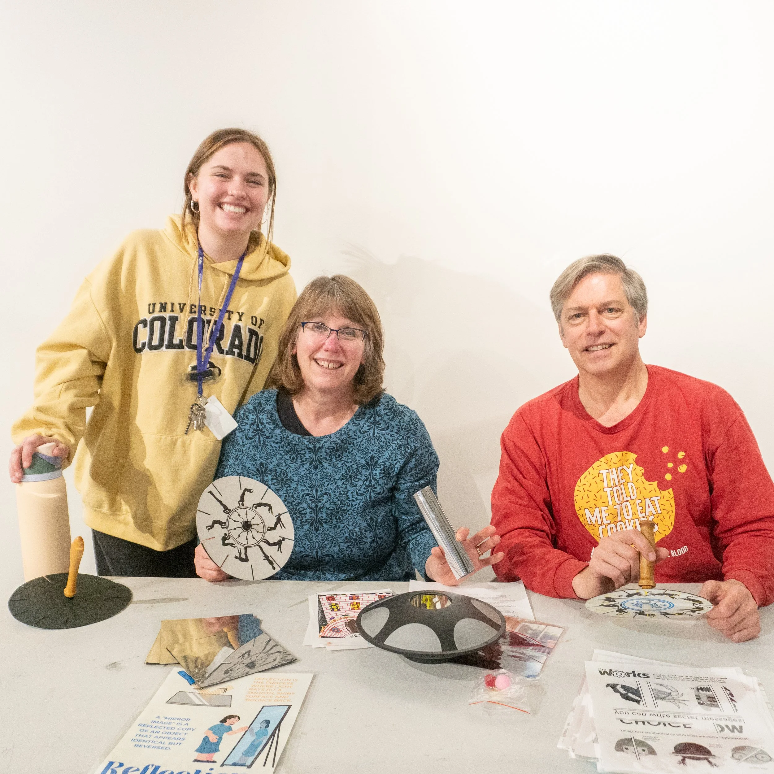 People gathered around a table with educational materials, posters, and games, engaged in an activity or workshop in a classroom or community space.