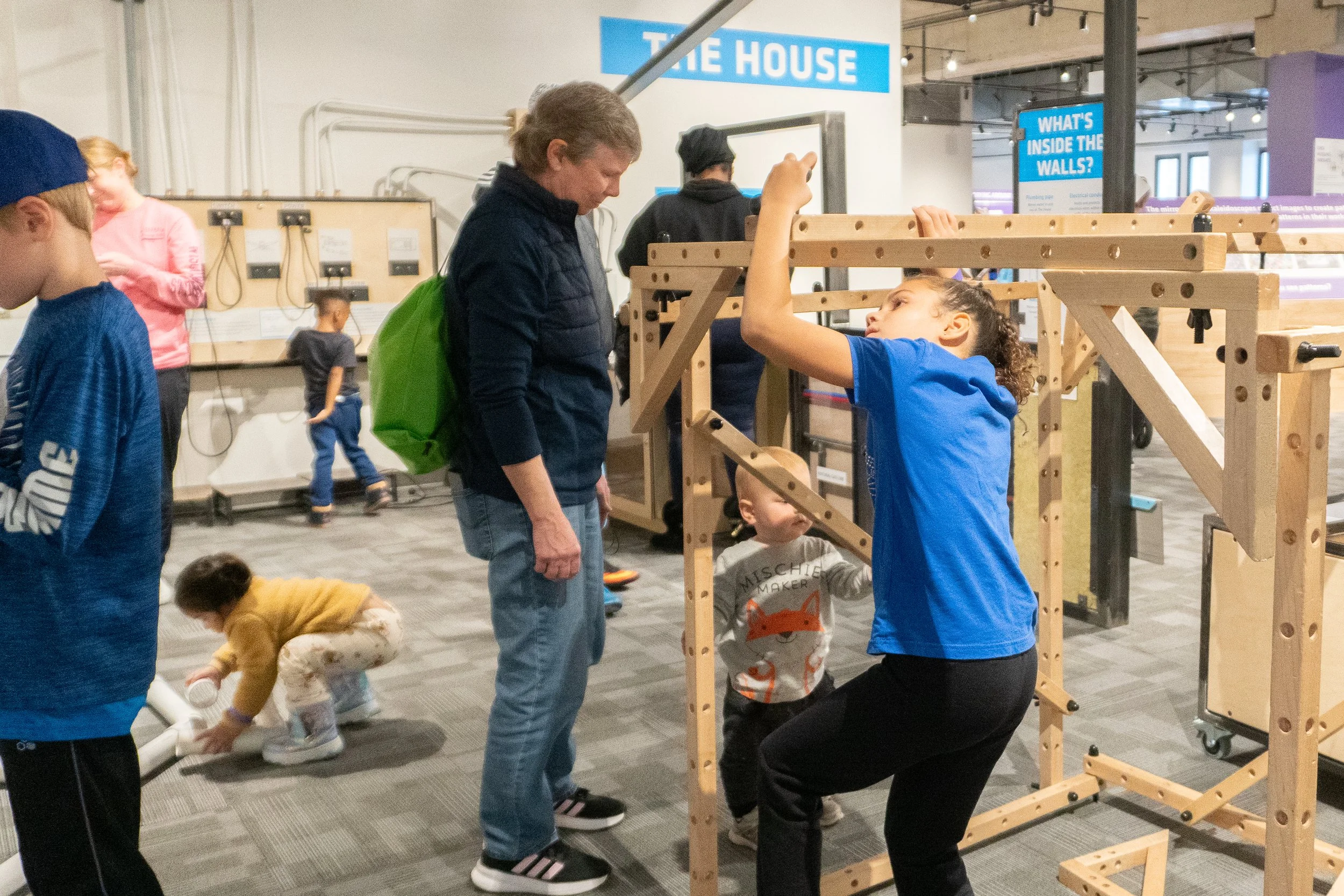 Children and an adult engaging with a wooden structure at an indoor science museum exhibit.