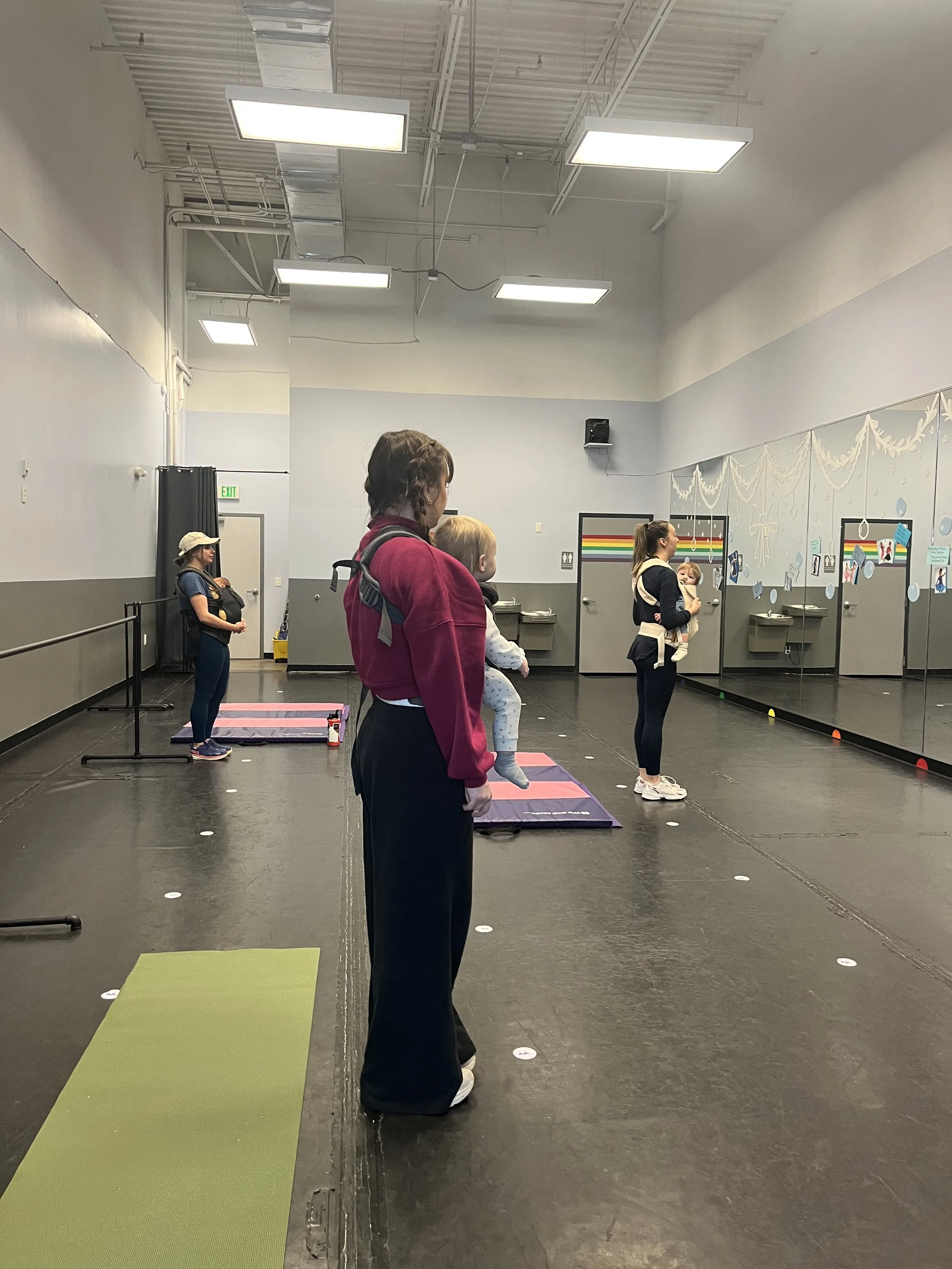 Parents with children practicing dance or exercise in a studio with mirrors and decorations on the wall.