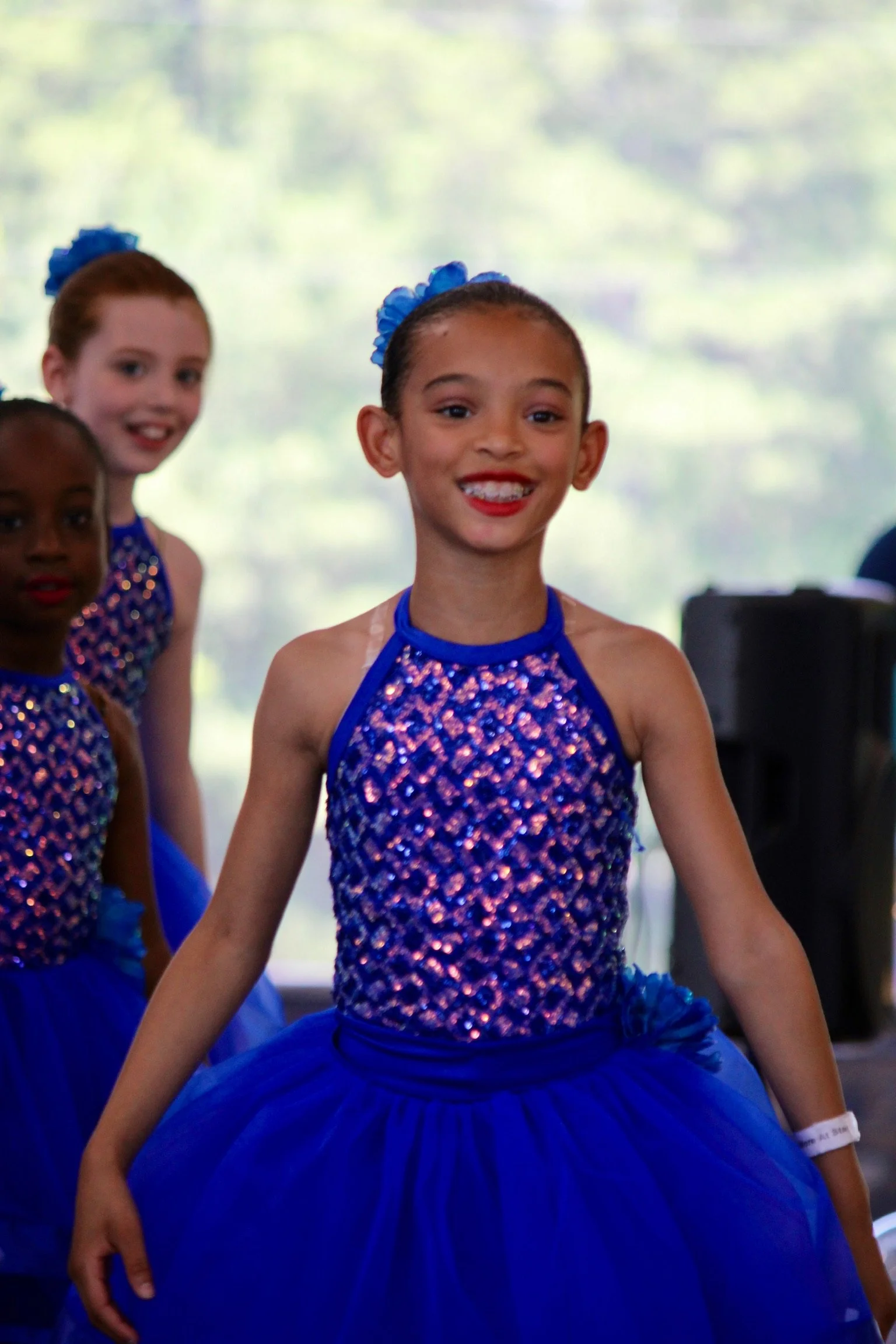 Group of young girls wearing matching blue and purple dance costumes, smiling.