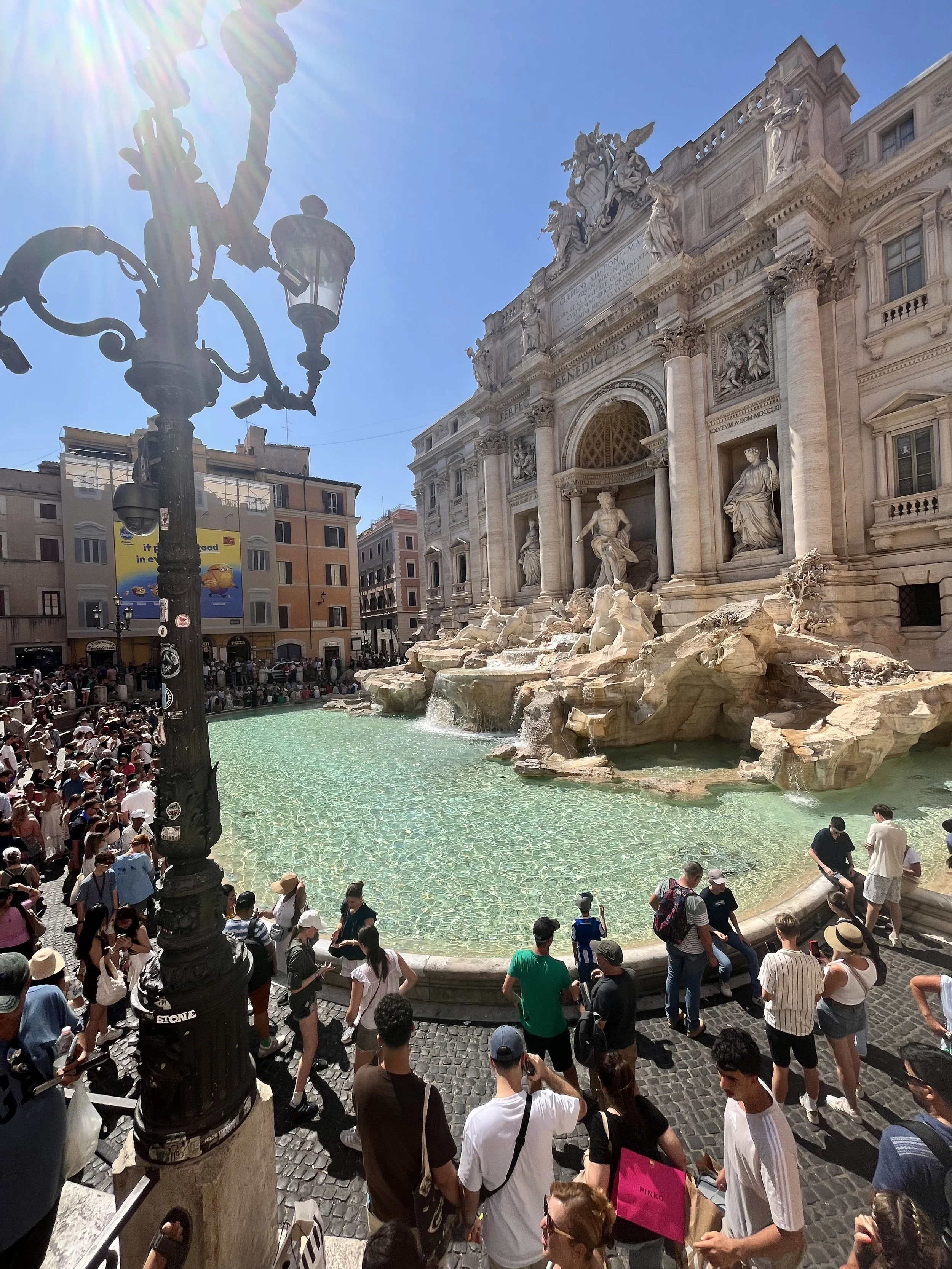 Crowd of tourists around the Trevi Fountain in Rome, Italy, on a sunny day.