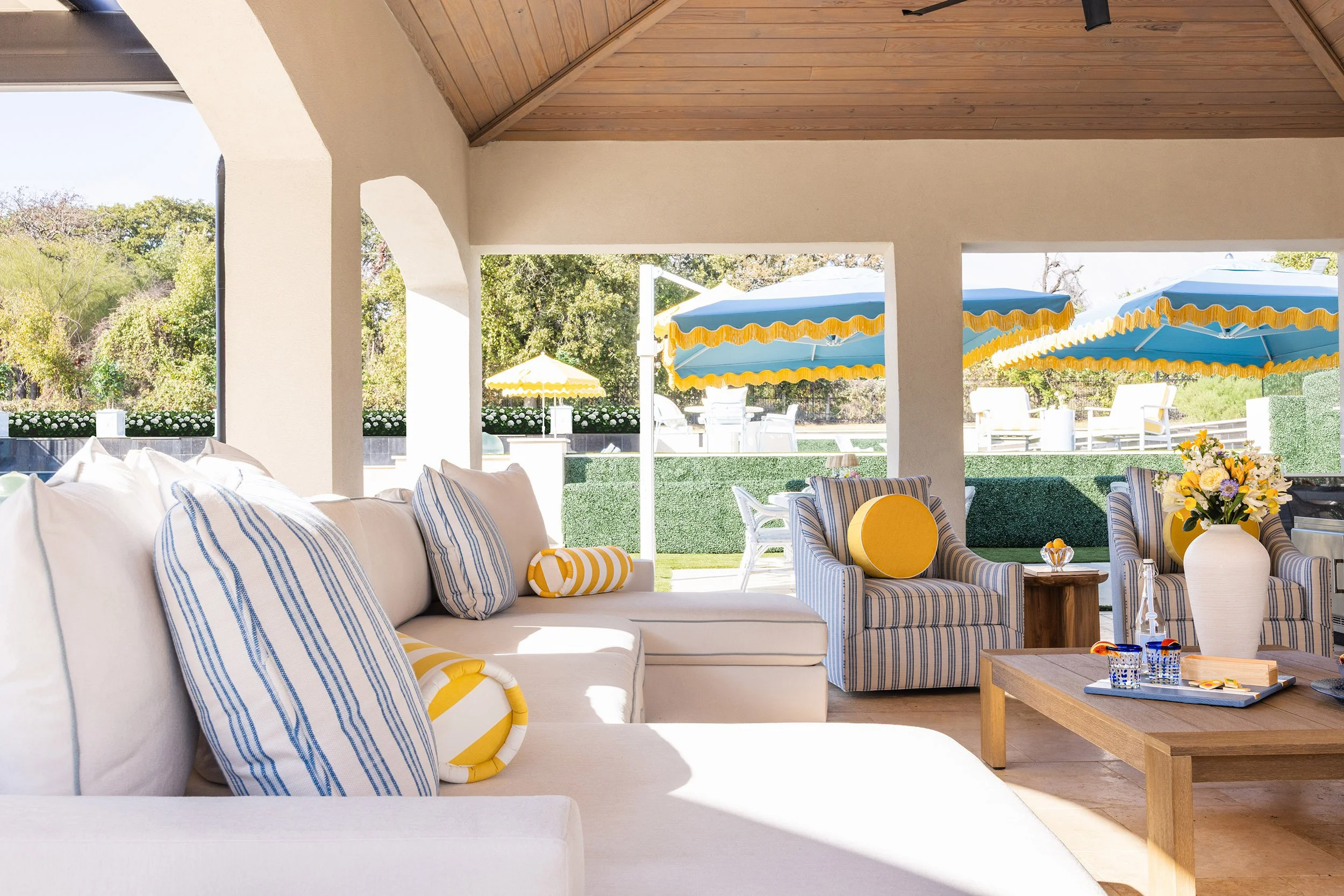 Covered outdoor patio lounge with white sectional sofa and striped armchairs for the Shady Oaks project designed by Dana Wiseman Design
