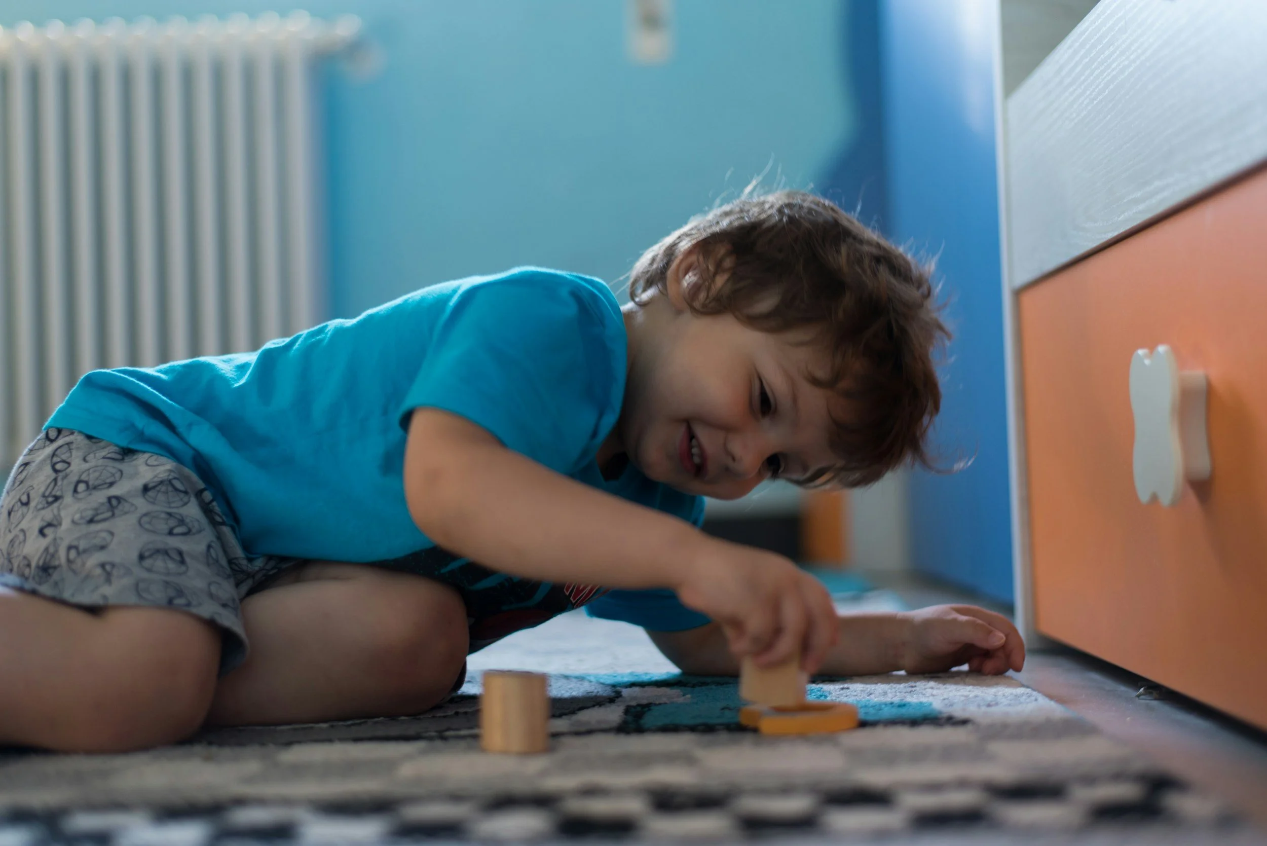 Young boy playing with wooden toys on the carpet in a colorful room.