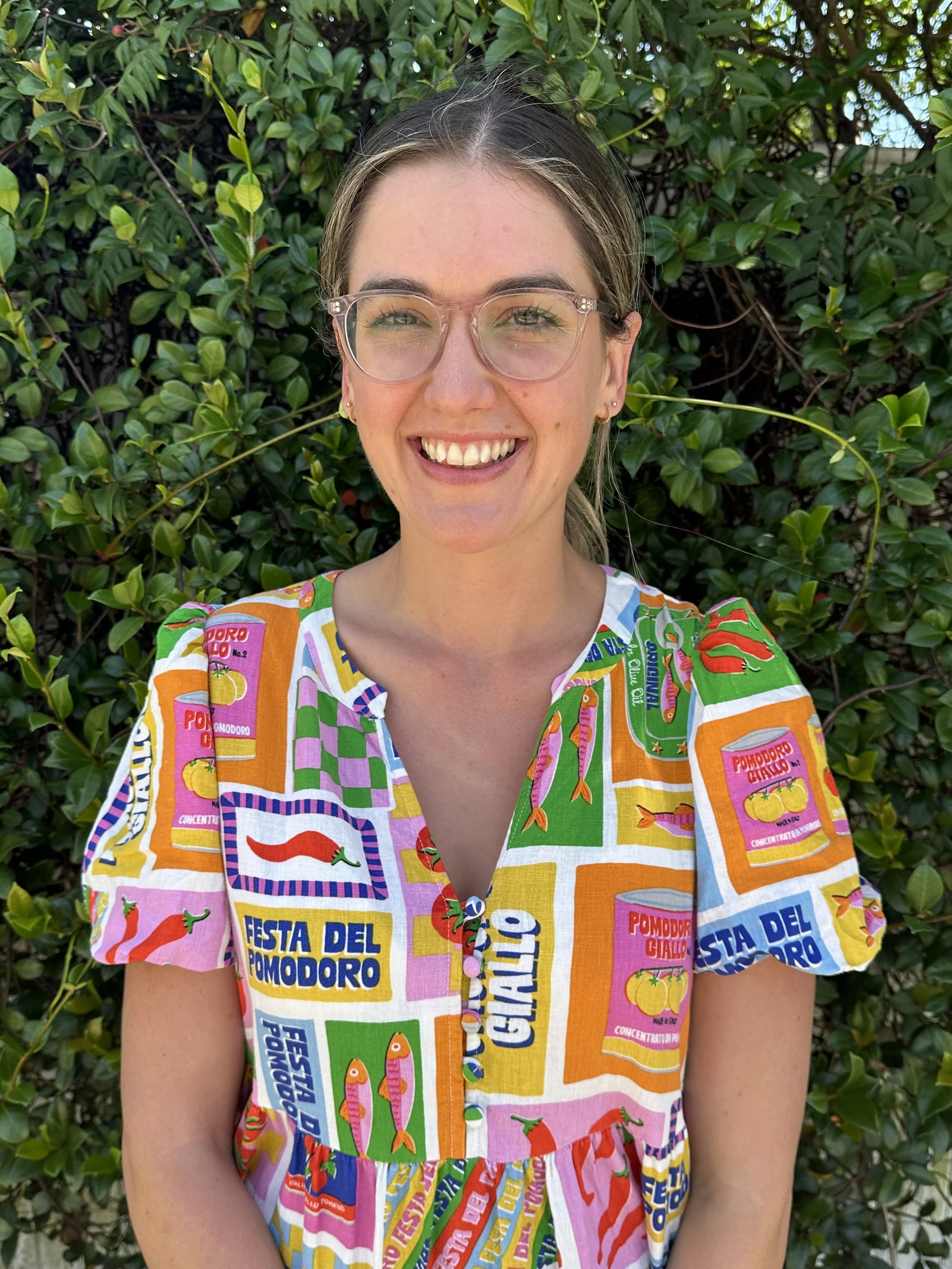 Heidi is wearing a colourful dress, clear rimmed glasses and is smiling in her friendly and approachable self looking directly at the camera.