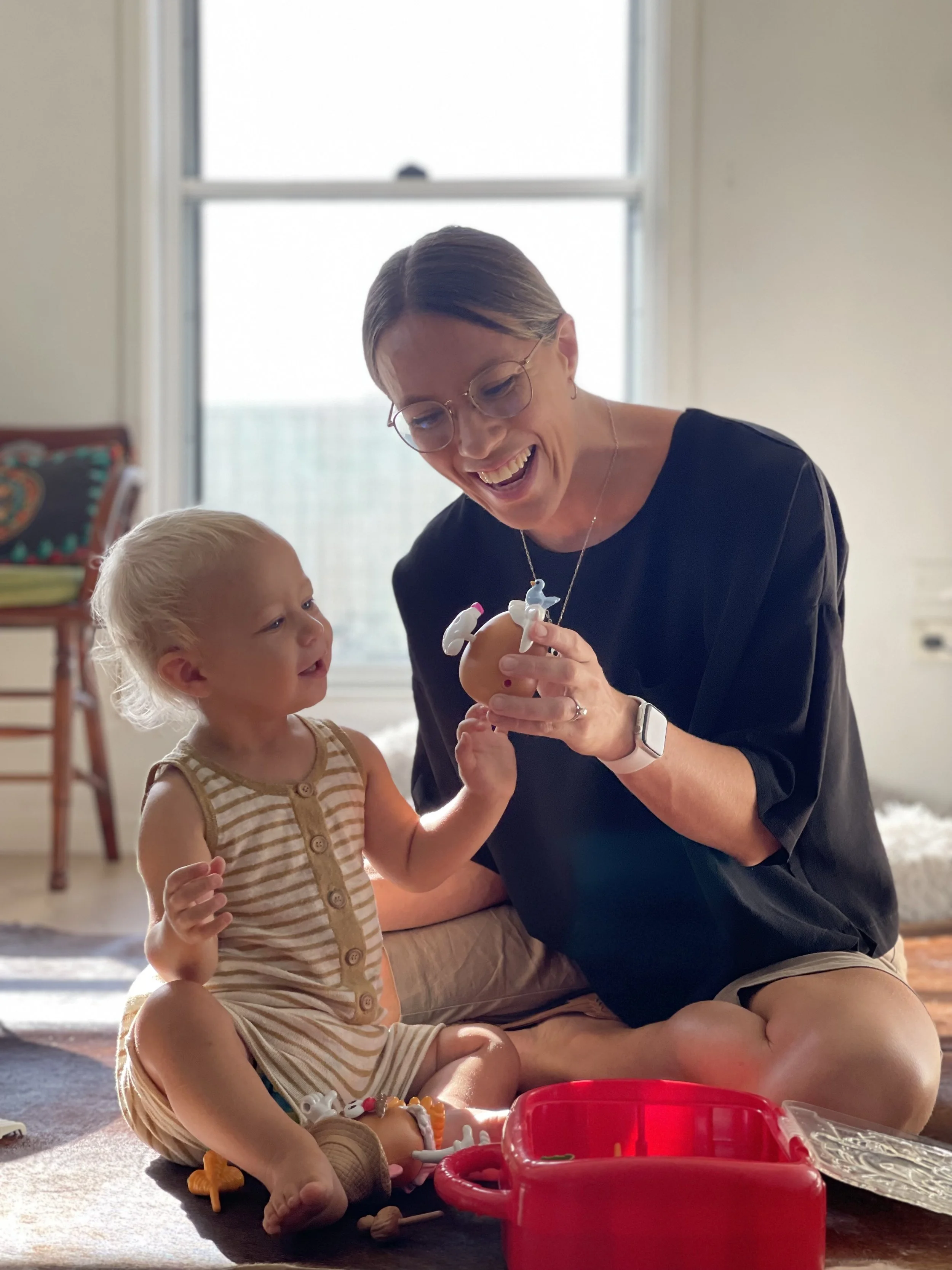 A therapist from Kids + Co.Lab is smiling playing with a toddler. They are both warmly engaged in play during an Occupational Therapy session.