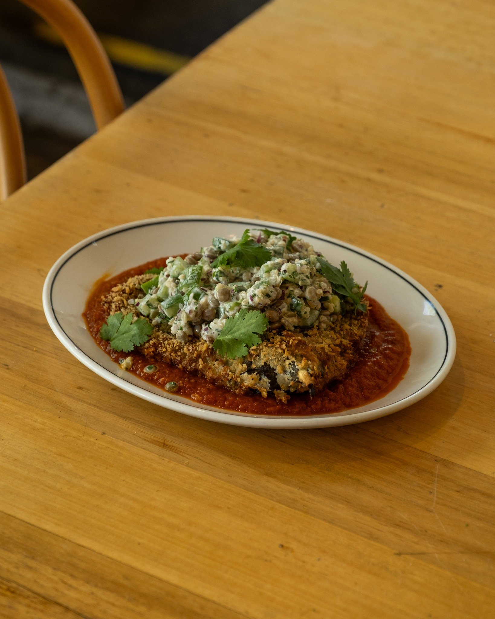 The dish is a delightful blend of flavors: cardamom-spiced crumbed eggplant provides warmth, while tangy tomato passata and hearty lentil quinoa salad add depth. A zesty lemon tahini dressing ties it all together.