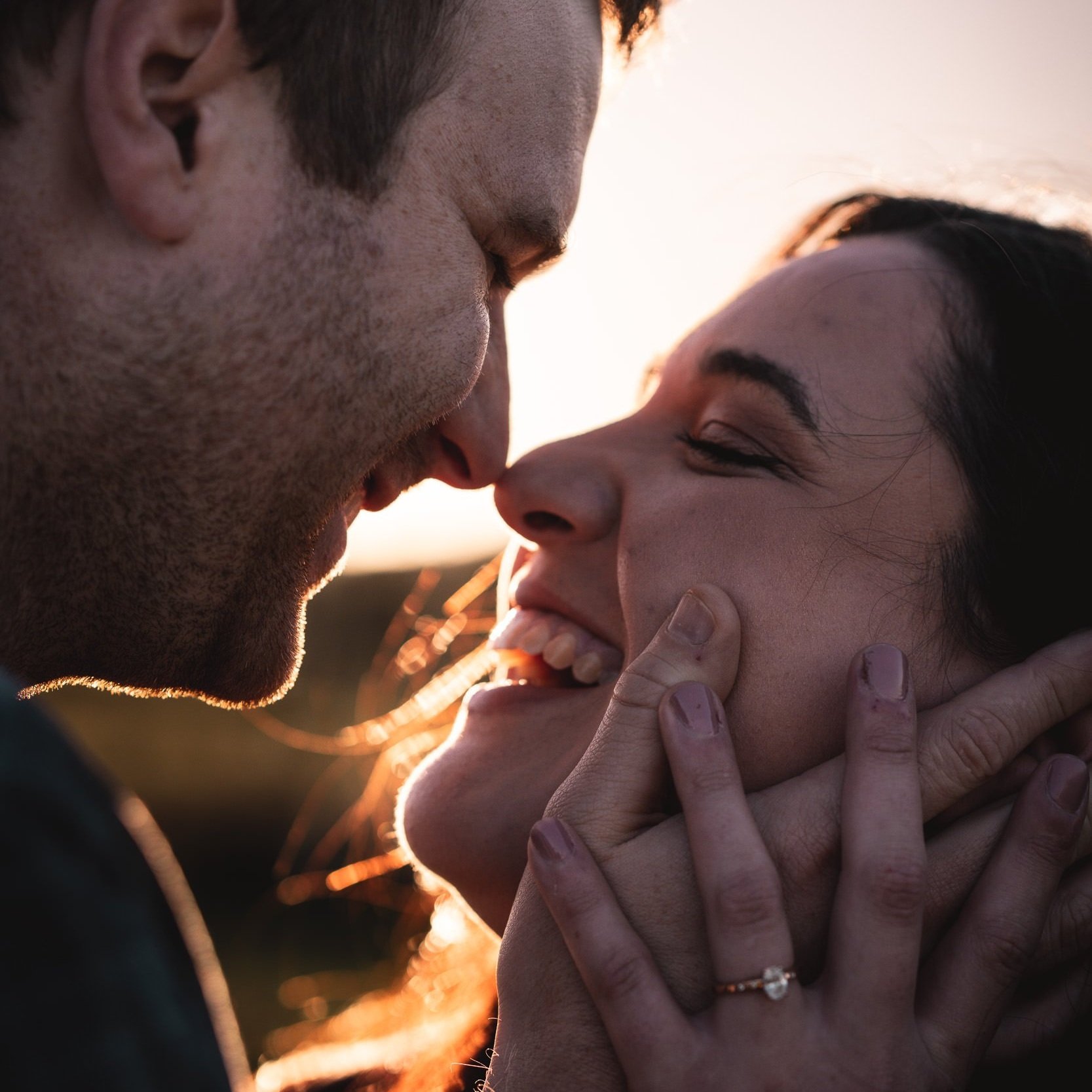 Close-up of a couple smiling and about to kiss, with woman wearing an engagement ring.