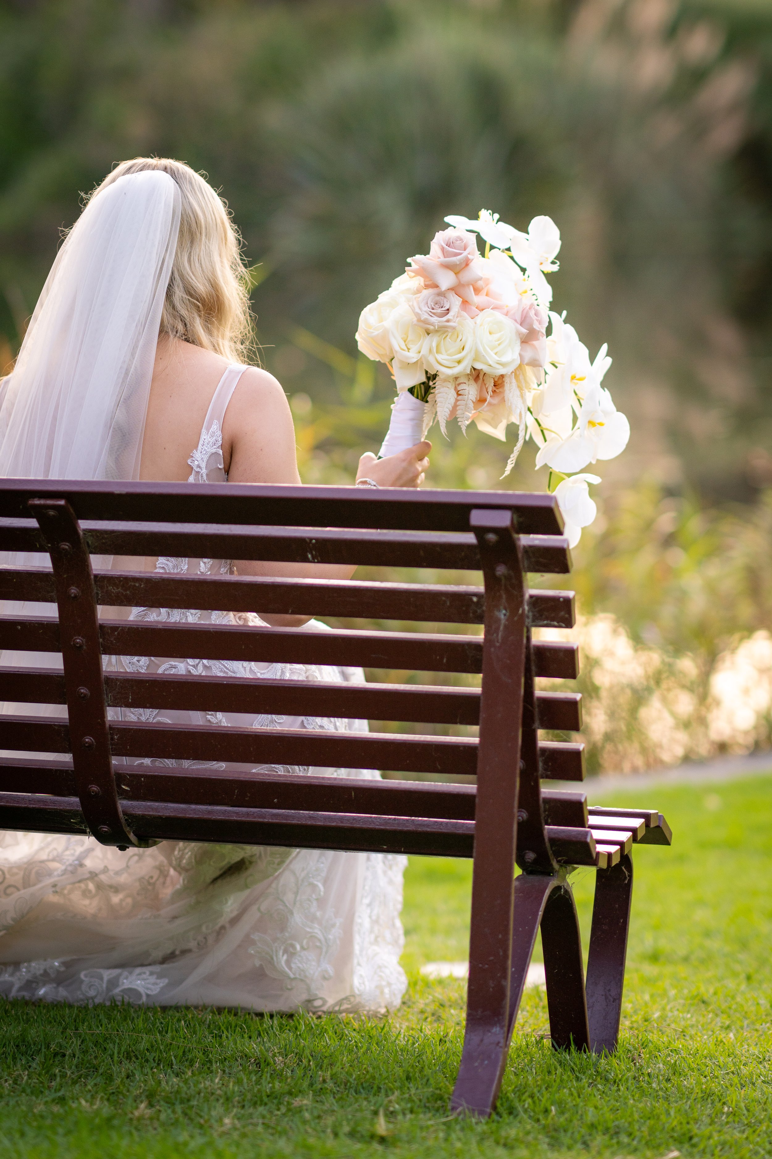 Bride sitting on a bench holding a bouquet of white and pink flowers.