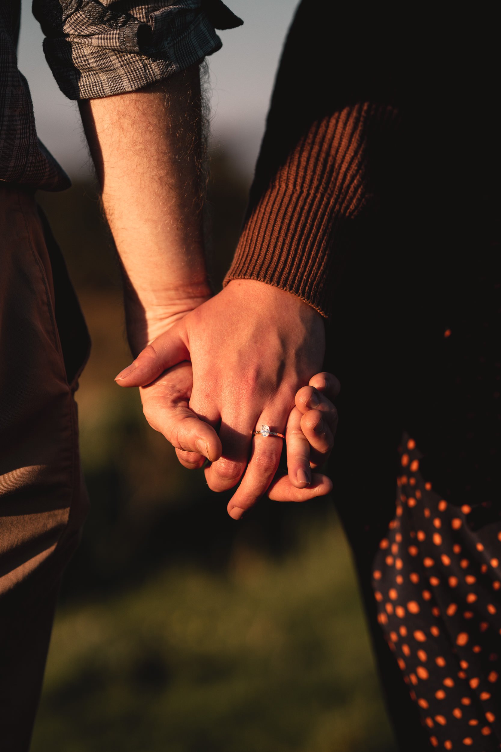 Two people holding hands with an engagement ring visible.