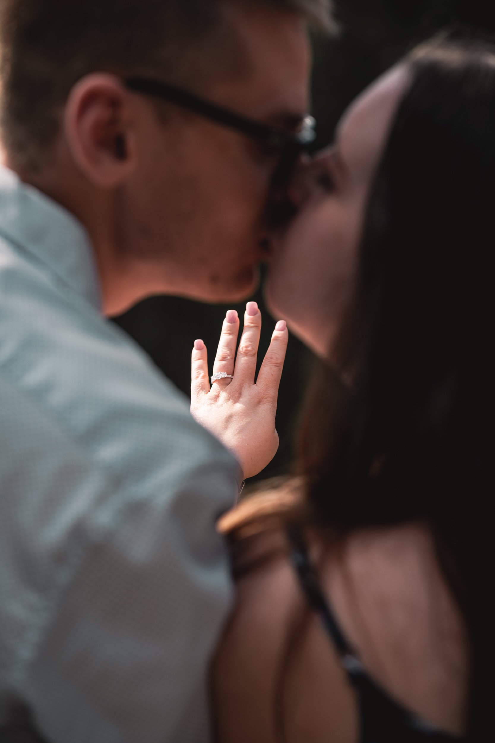 Couple kissing with visible engagement ring on woman's hand.