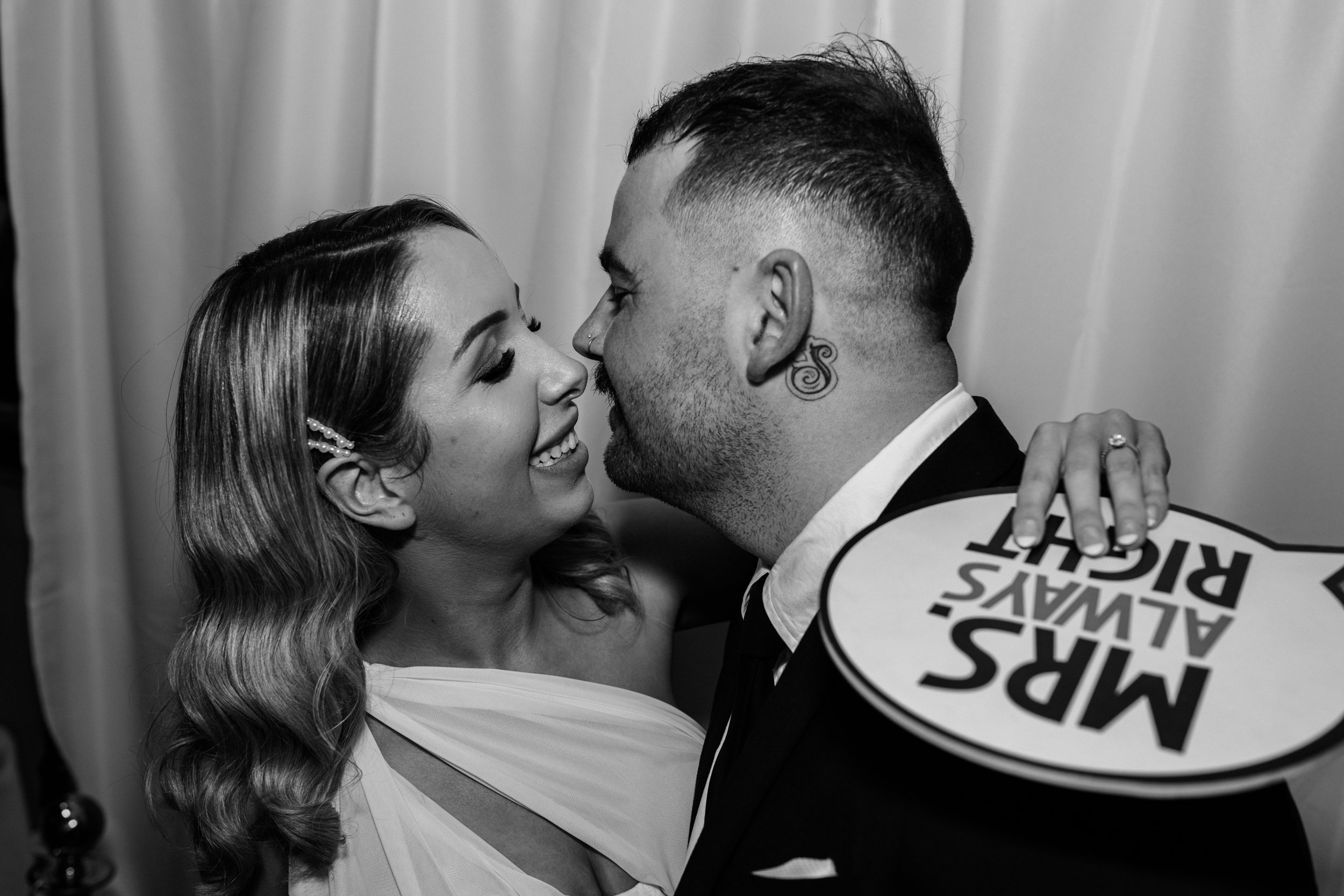 Black and white photo of a couple smiling closely with a sign that reads 'Mrs. Always Right'.