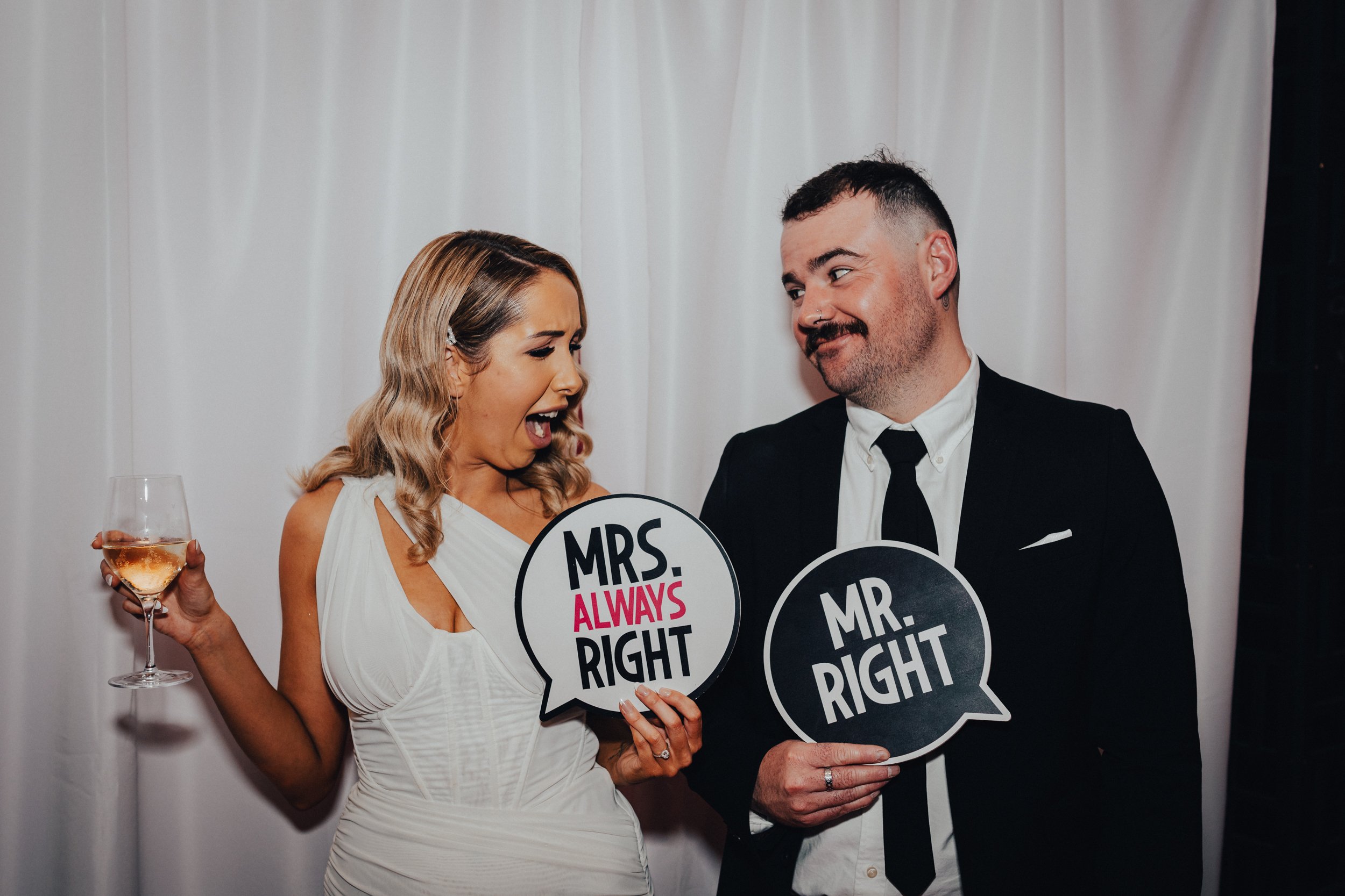 Couple in formal wear holding funny signs that say "Mrs. Always Right" and "Mr. Right" at an event.