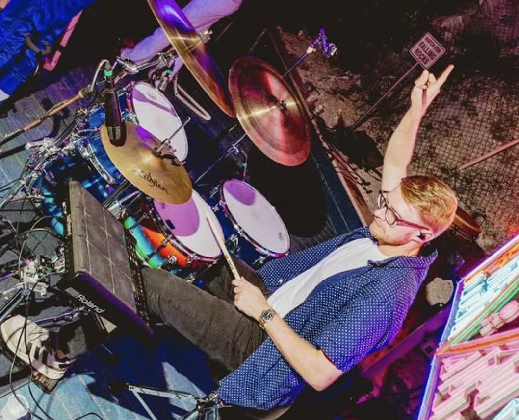 A man playing a drum set in a room with colorful neon lights.
