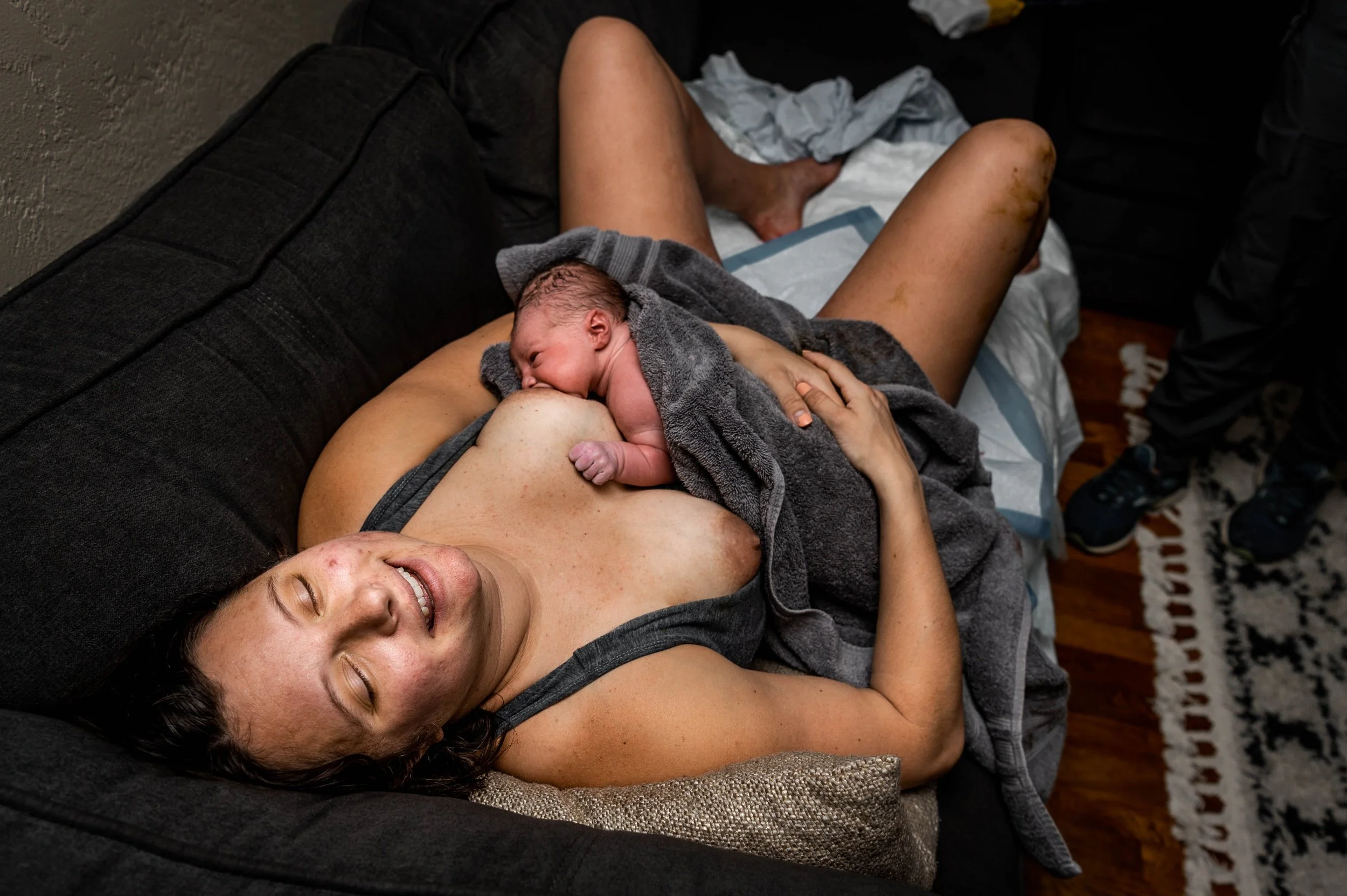 Mother holding newborn baby on the couch, smiling after giving birth at home