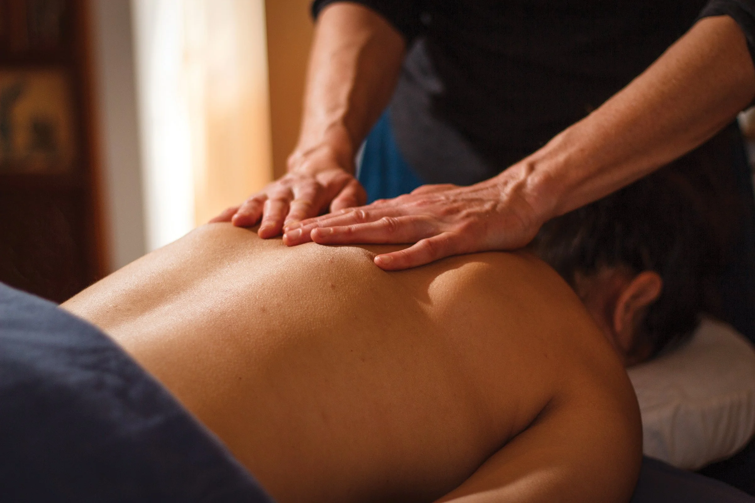 A person receiving a back massage from a massage therapist in a warm, indoor setting.