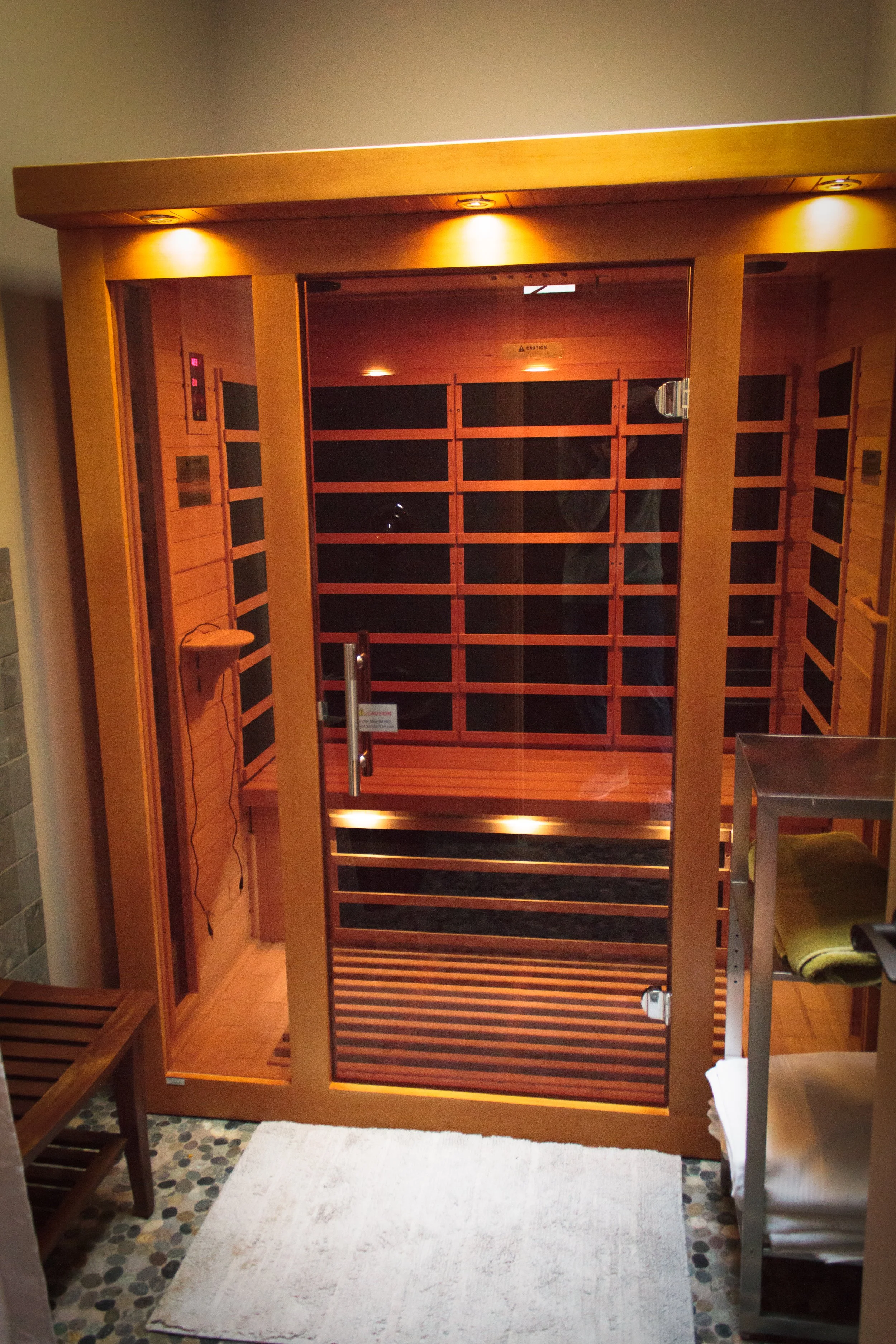 Inside a wooden infrared sauna with a glass door, bench, and dim lighting.
