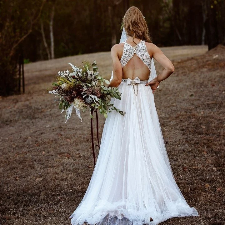 Back view of a custom bridal gown showcasing intricate lace detailing and an elegant open-back design, photographed on a real bride.