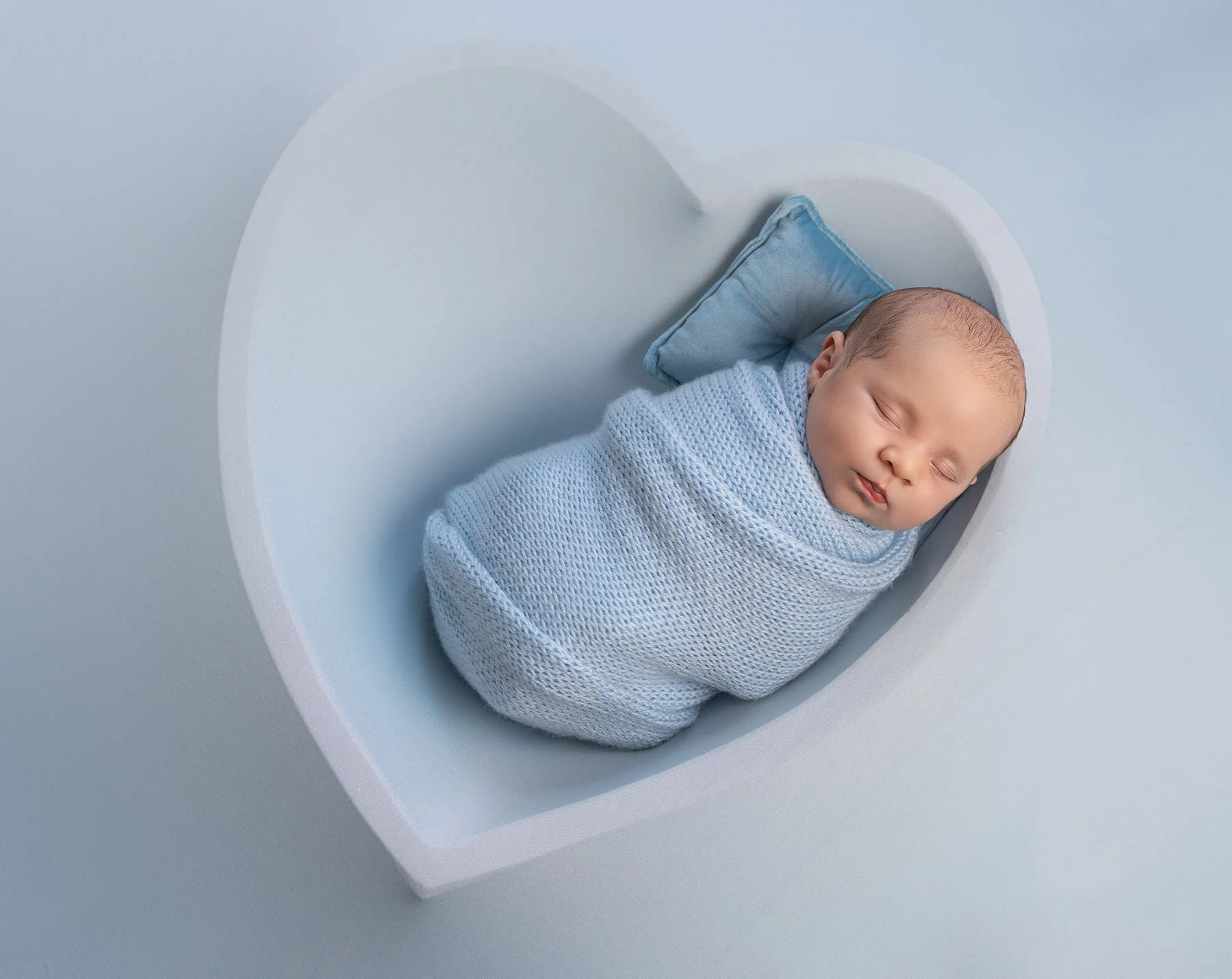 baby wrapped in baby blue placed in a heart bowl