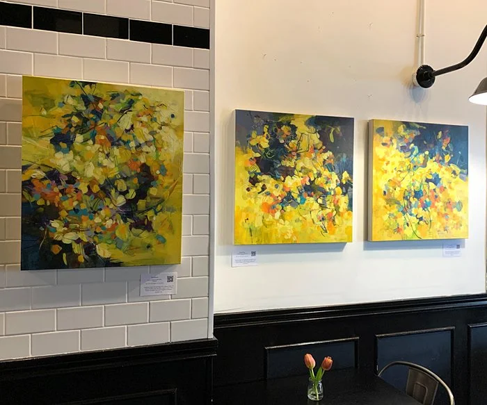 An installation of yellow abstract paintings on a wall in a restaurant.