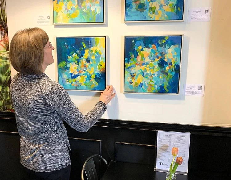 The artist hanging four square paintings together on a wall.