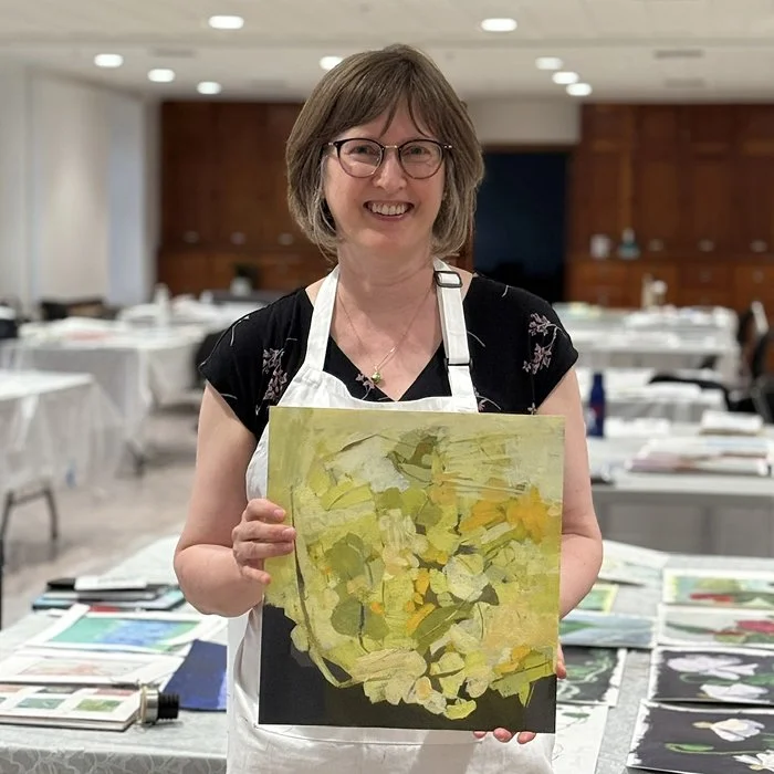 The artist as student holding a mostly yellow painting on paper.