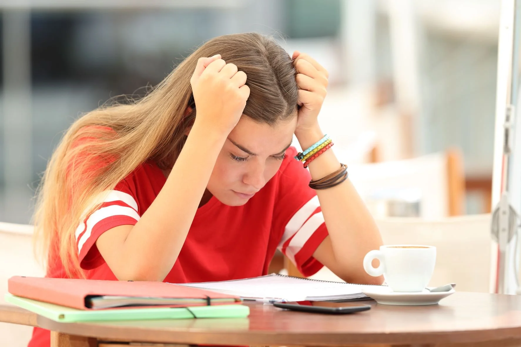 Female student sitting at table with coffee struggling over homework and stress