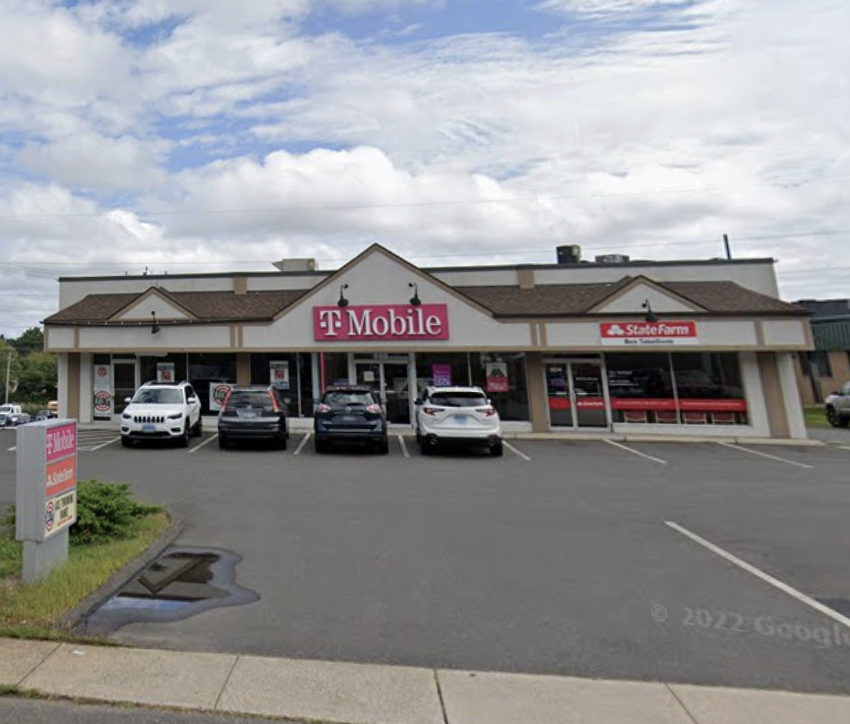 Front view of a strip mall with T-Mobile store, storefronts for A State Farm Insurance, and three cars parked in front on a cloudy day.