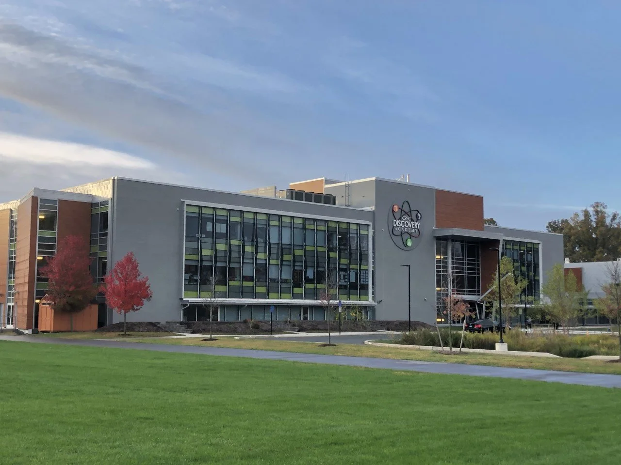 Exterior of Discovery Science Academy building with a grassy foreground, trees with autumn foliage, and a clear sky.