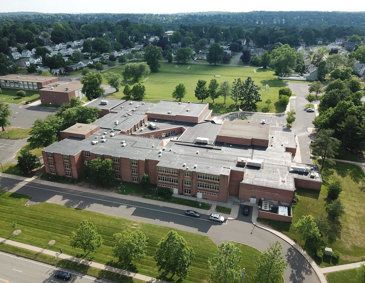 Aerial view of a school building with a sports field and residential neighborhood in background.