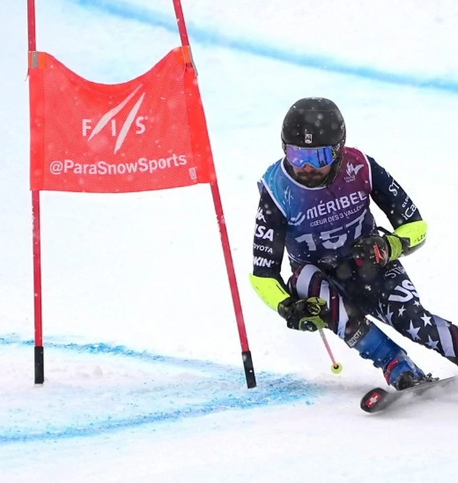 Tyler McKenzie racing giant slalom past a red FIS gate in Méribel, France, one pole in his right hand