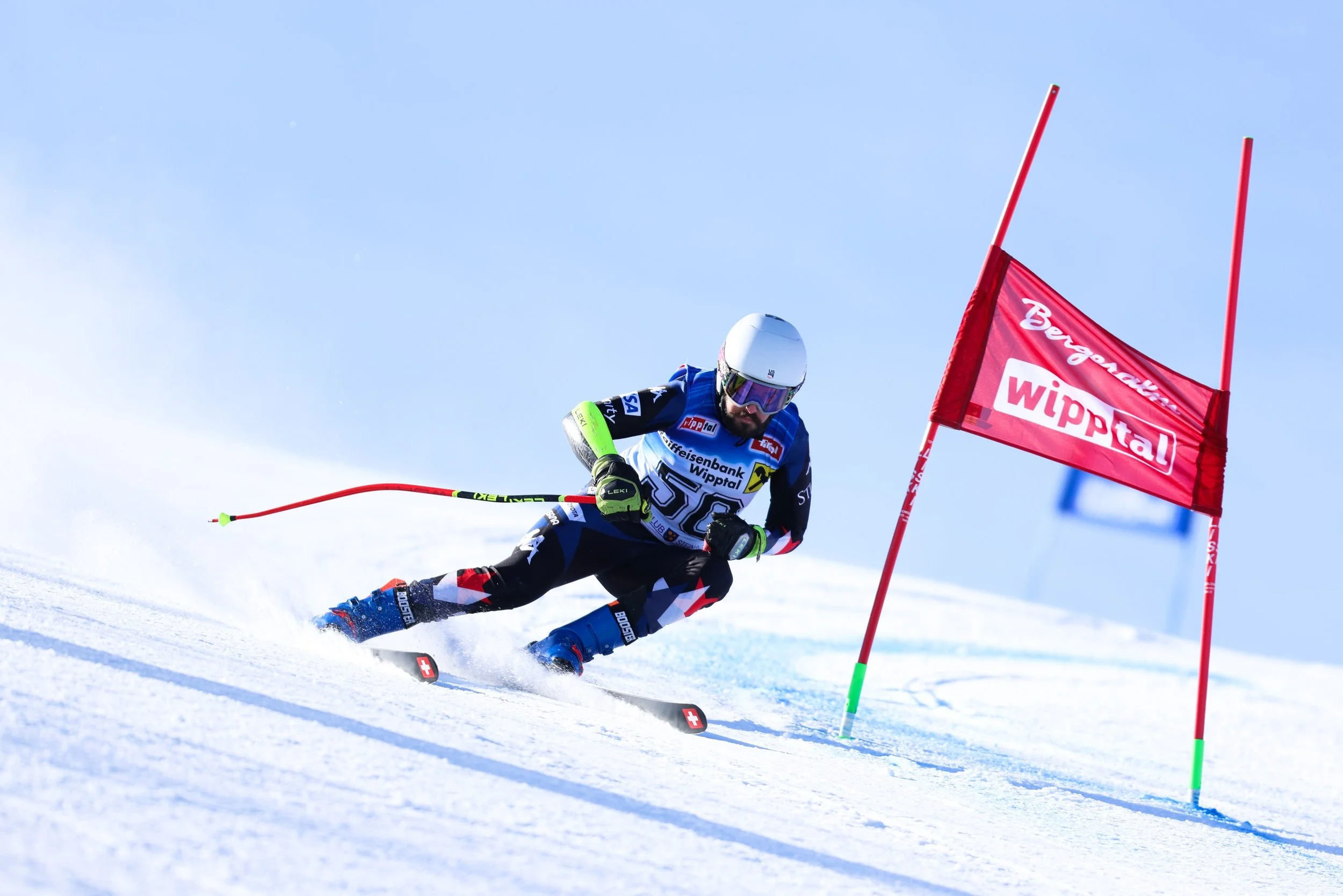 Giant slalom past a red gate, one pole in his right hand