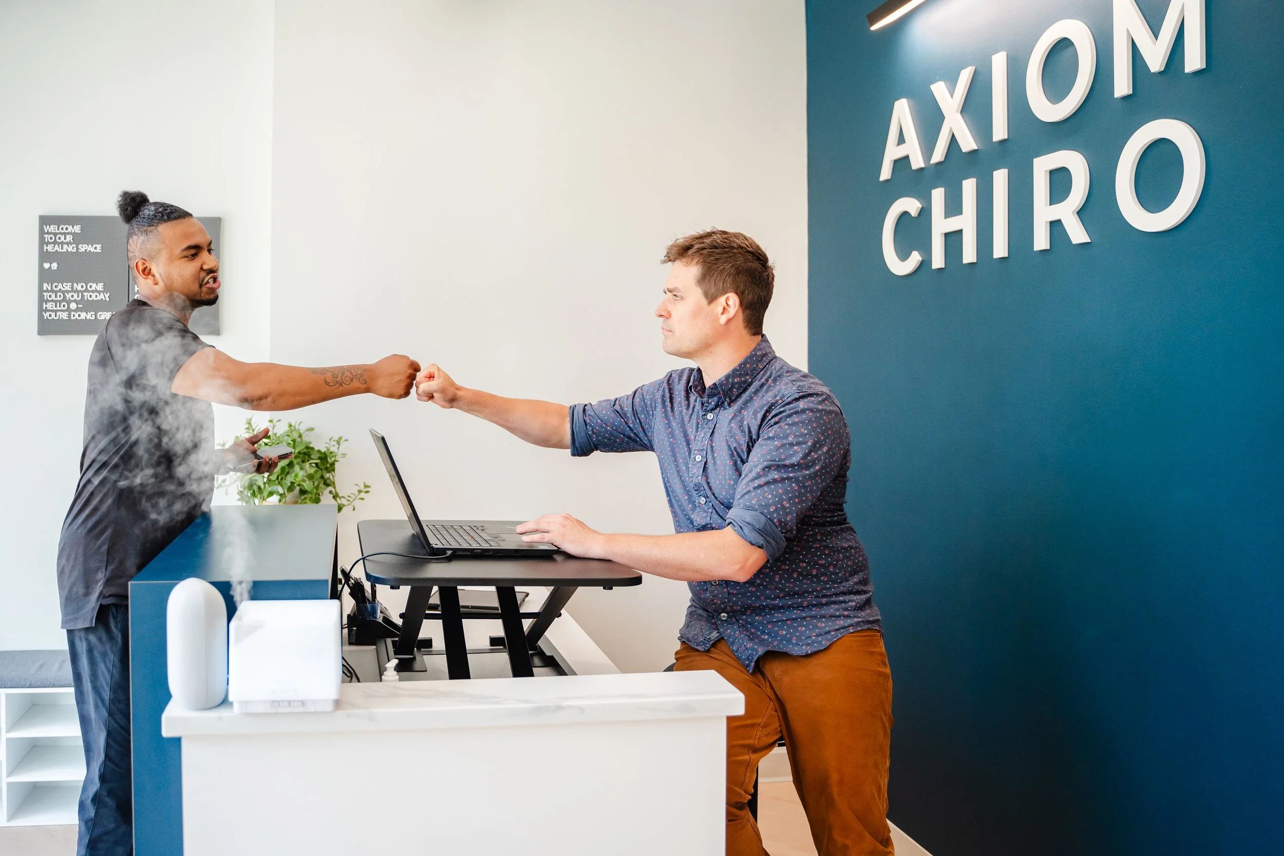 Calgary chiropractor greeting a patient at the front desk of Axiom Chiropractic, showcasing a welcoming and modern chiropractic clinic.