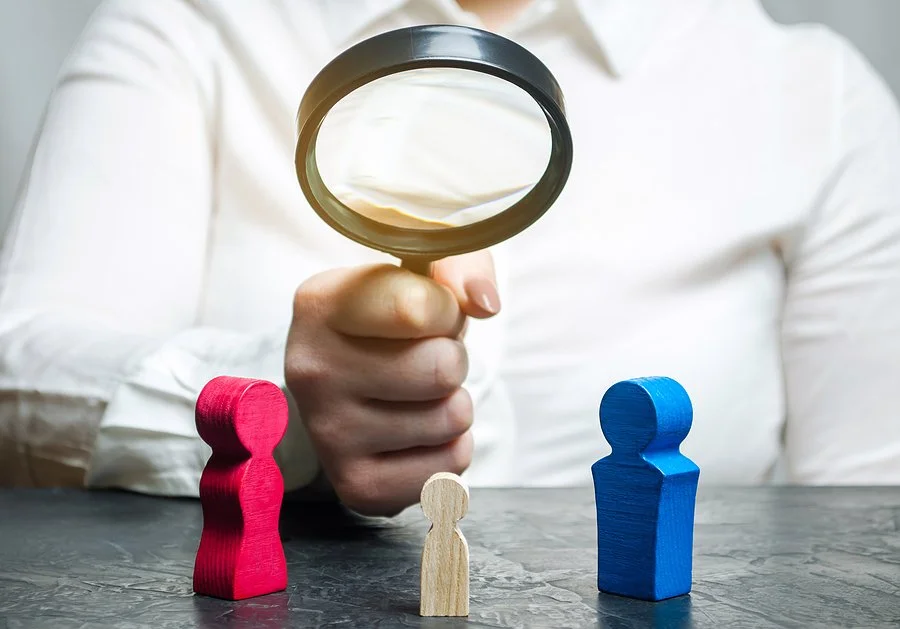 A magnifying glass over wooden figurines representing a mother, father, and child, symbolizing child custody evaluation and legal scrutiny during a divorce or family court proceeding