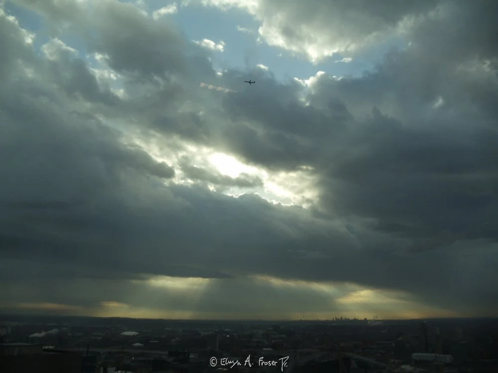 View 404 - distant plane flying high across clouds exploding with sun beams overlooking urban area, Humanity, Wildlife, Spring 2015