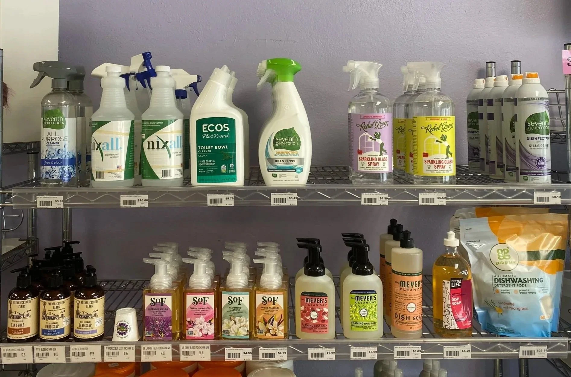 Shelves of cleaning products including disinfectants, sprays, and hand soaps, with a purple sign reading 'Cleaning Products' on a light purple wall.