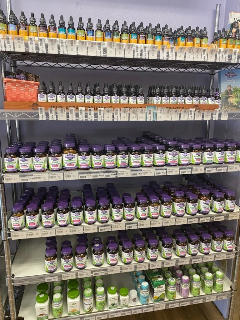 A metal shelving unit filled with various bottles of herbal supplements or vitamins, organized by type and size, with labels facing outward.