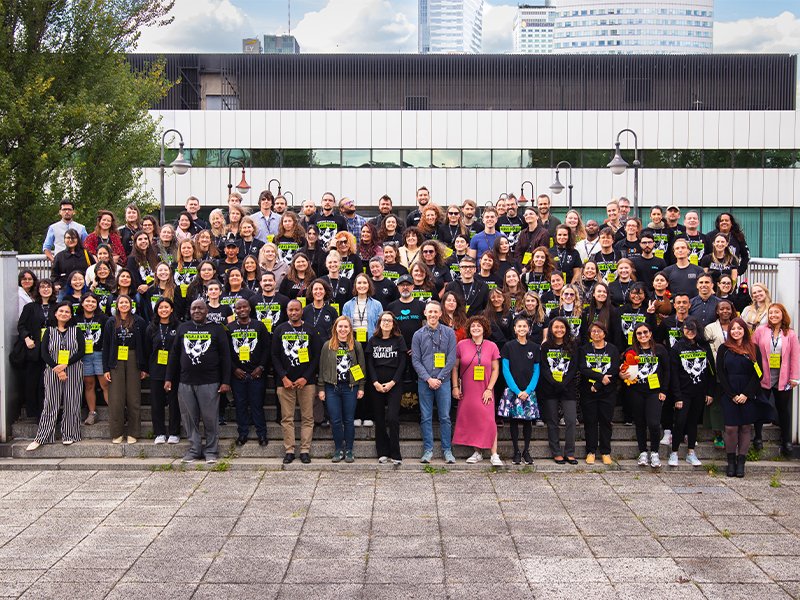Group of people gathered outdoors on steps in front of a building, posing for a group photo during daytime.