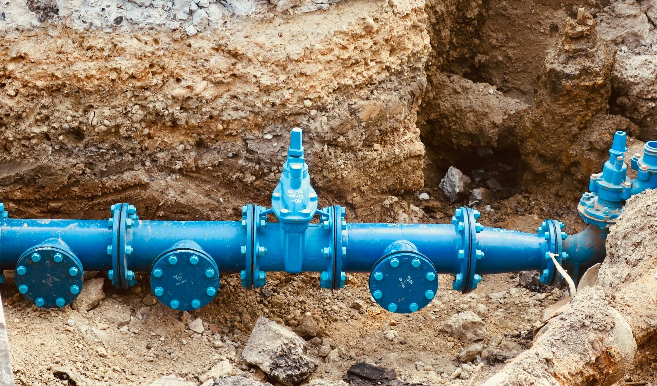 Blue water pipe with valves installed underground in a dirt excavation site.