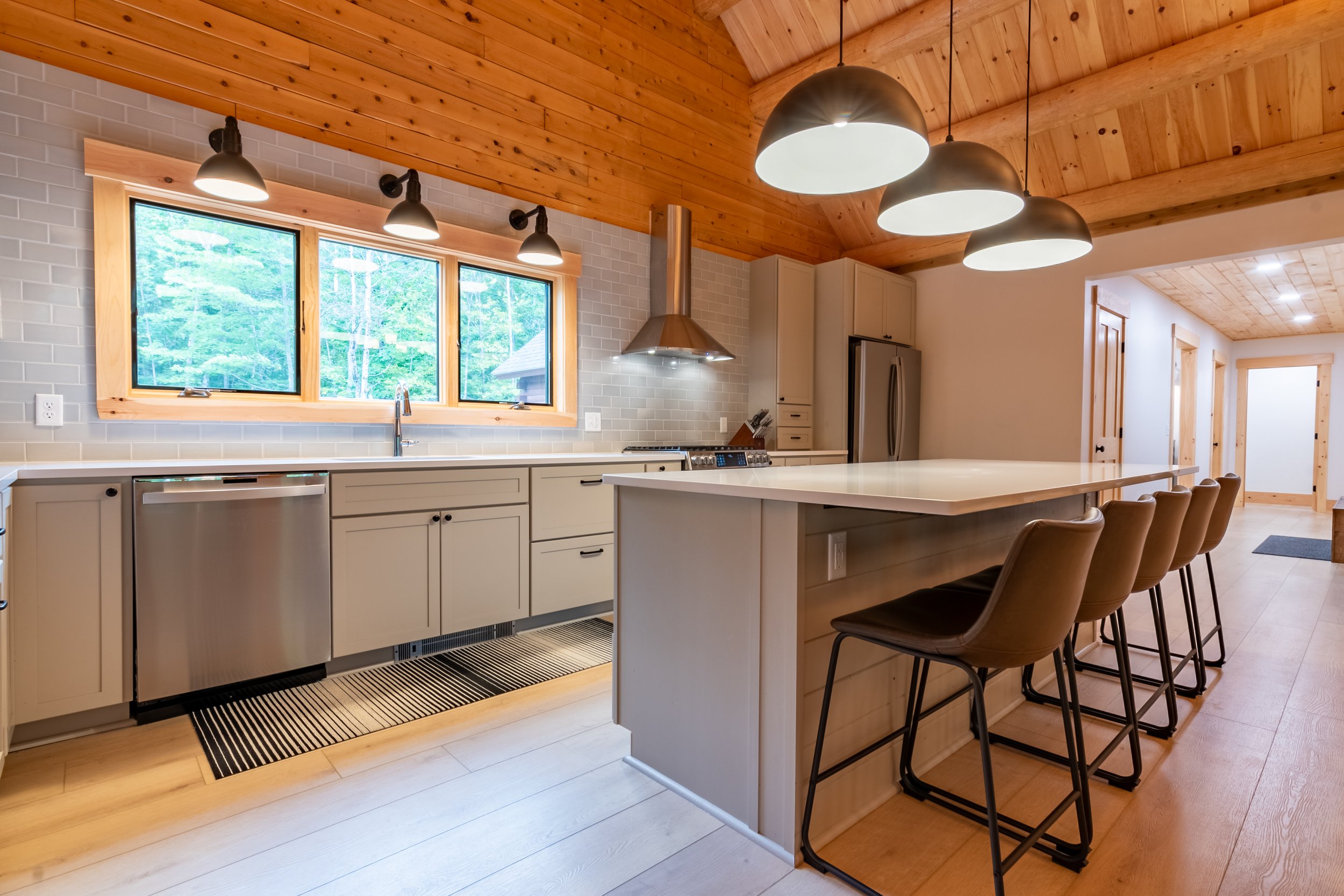 Large pendant lights centered on the island echo the smaller task lighting over the sink, creating a ceiling-like effect below the exposed beams.